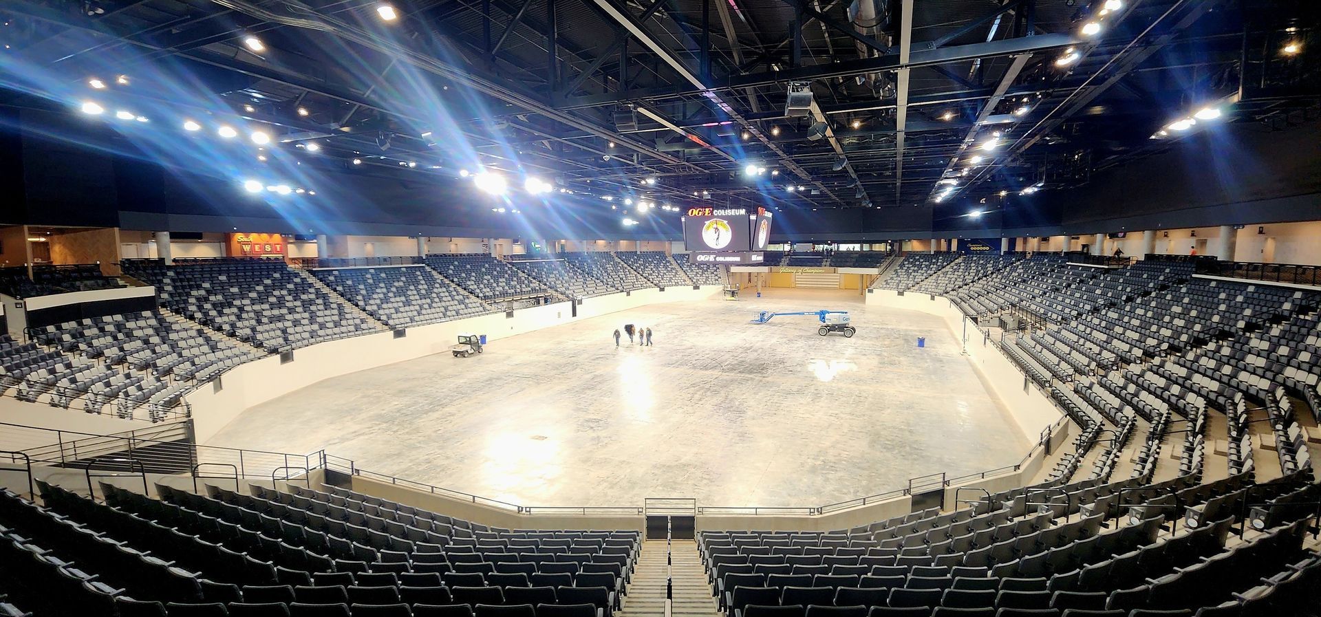 Large indoor equestrian arena with spectators in the stands, bright lighting focused on the dirt arena.