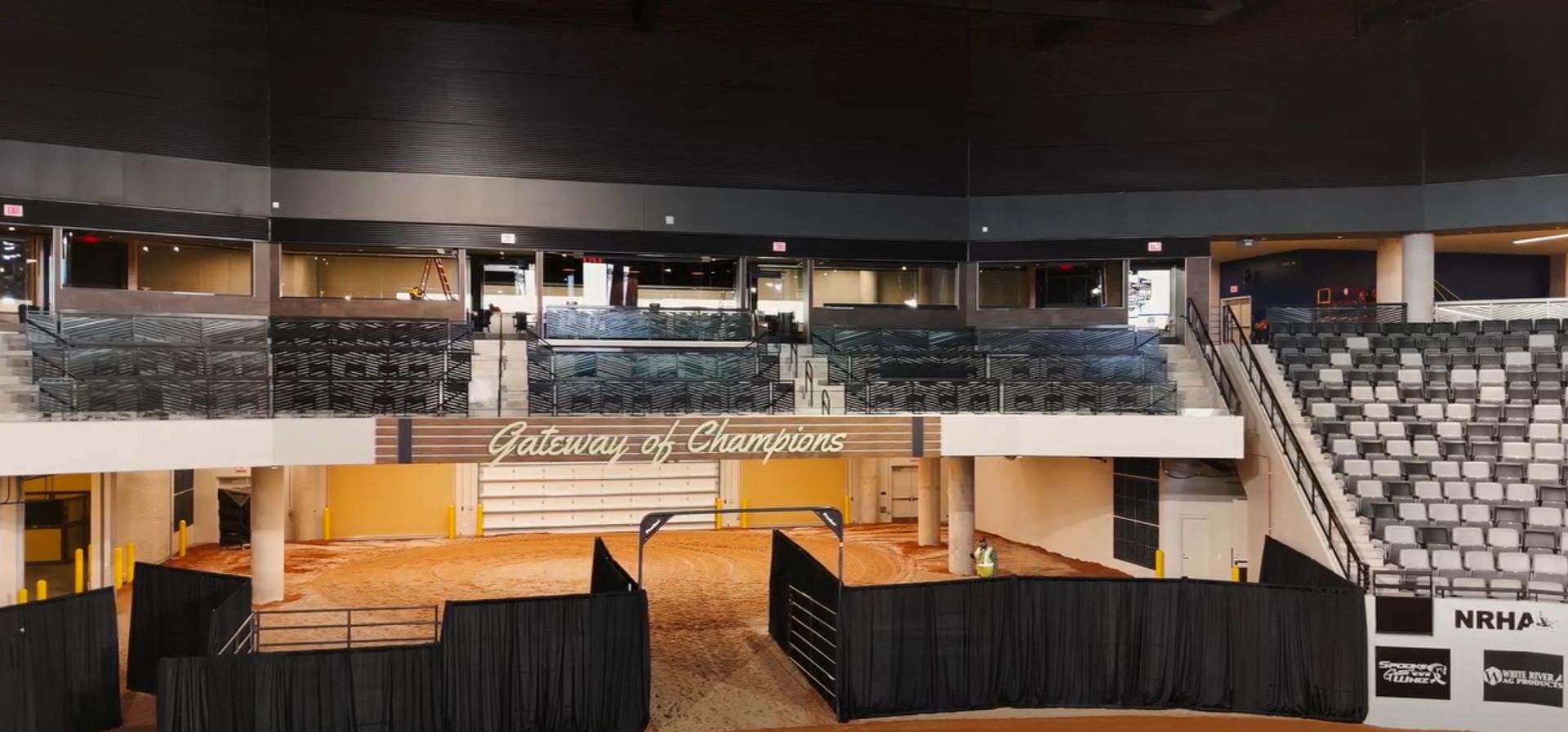 An indoor arena with black curtains, seating, and a dirt floor, 