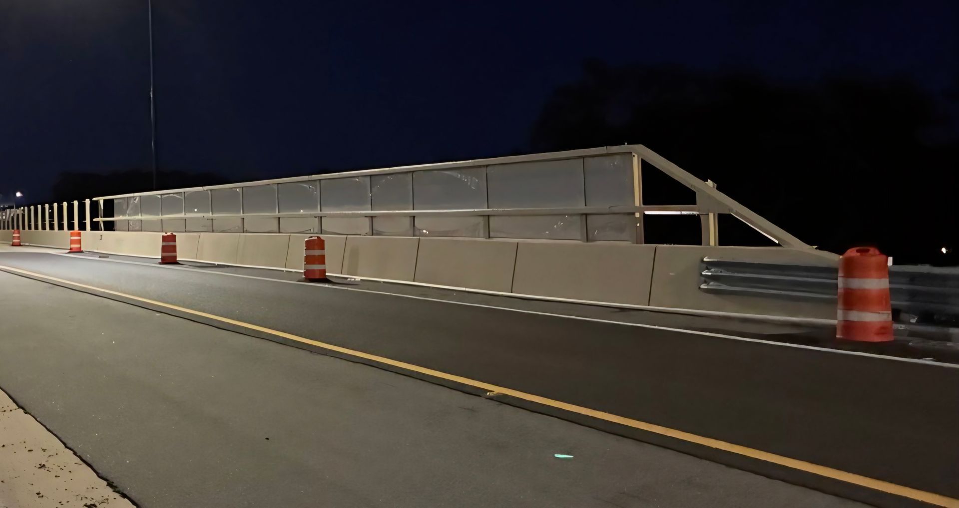 Concrete bridge side with metal supports and a streetlight under a blue sky.