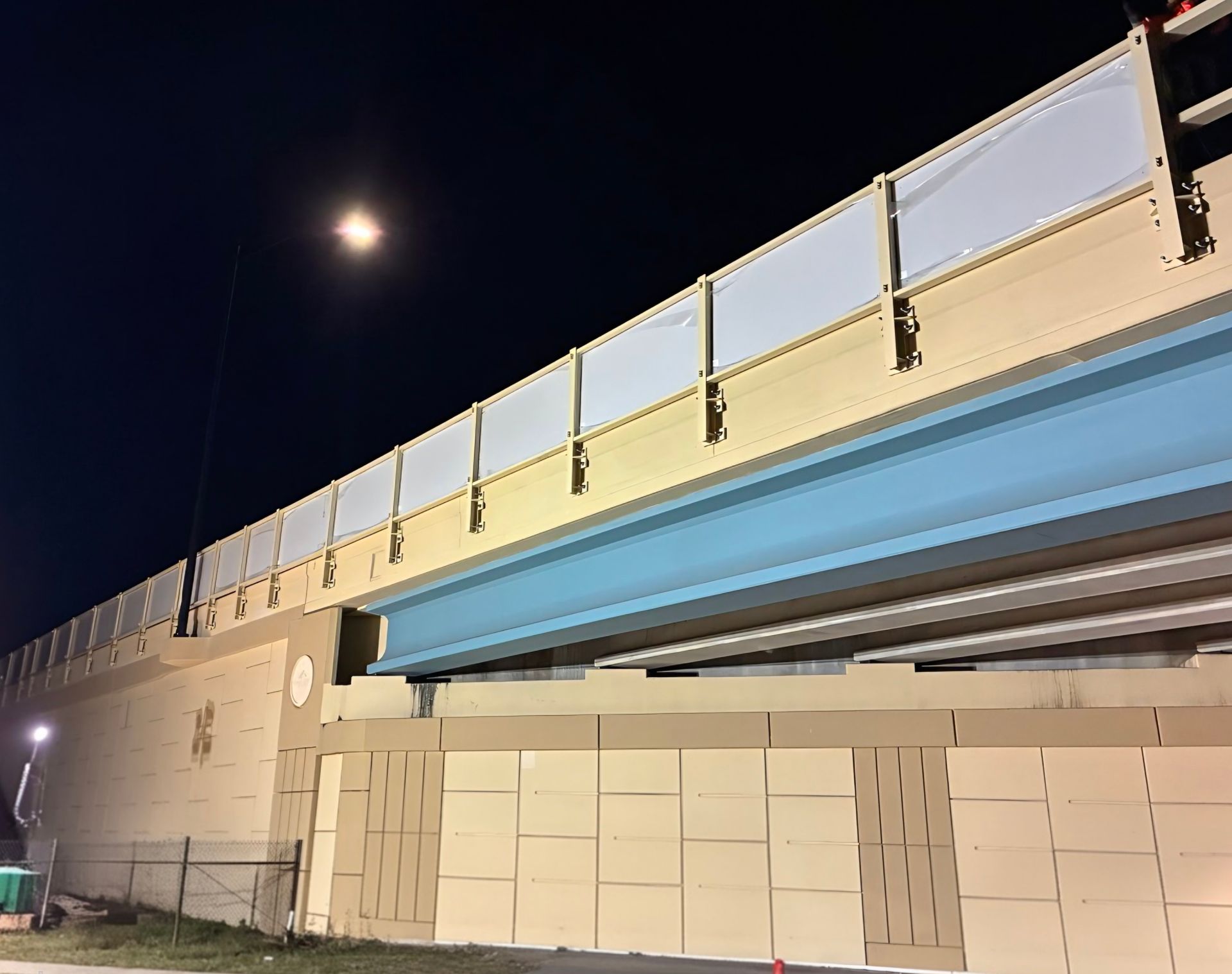 Bridge at night with safety barrier, lit by streetlight.