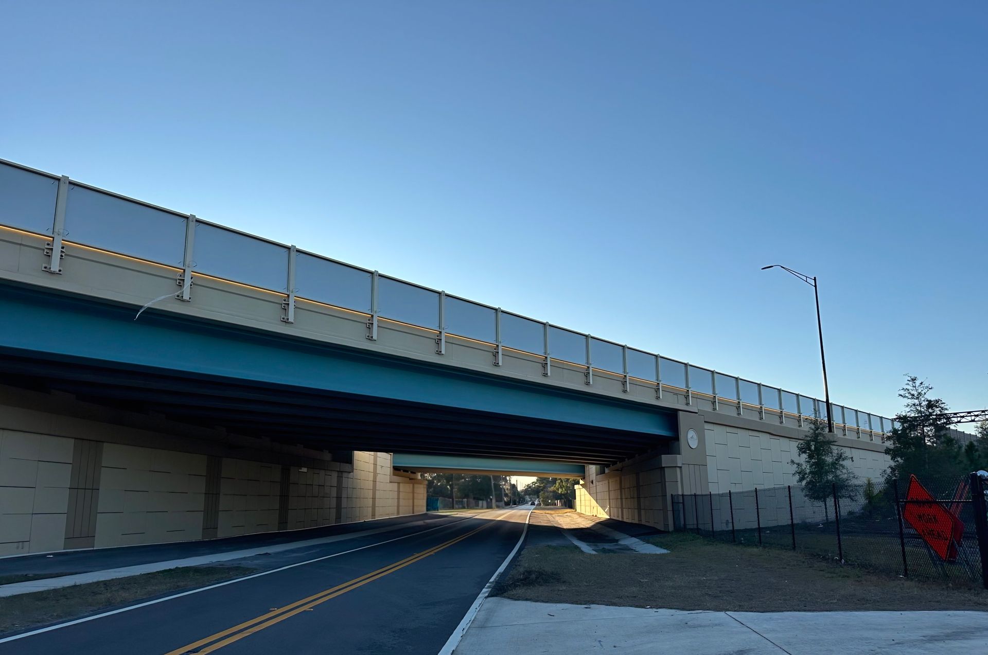 A road under a bridge with blue underside, clear sky, and a bike lane on the right.