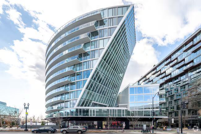 Modern curved glass and white building with a triangular glass section, next to a similar, smaller building.
