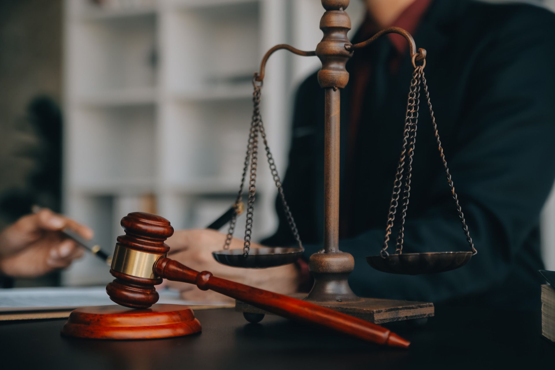 Gavel and scales of justice on a desk, lawyer in background, indoors.