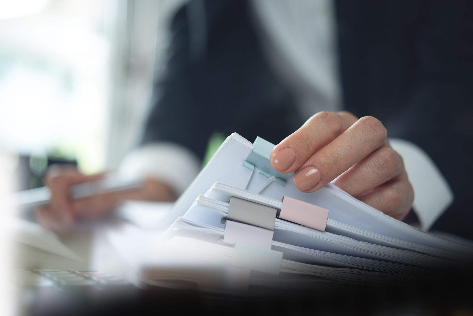 Person in a suit sorts through a stack of papers with colorful tabs, indoors.
