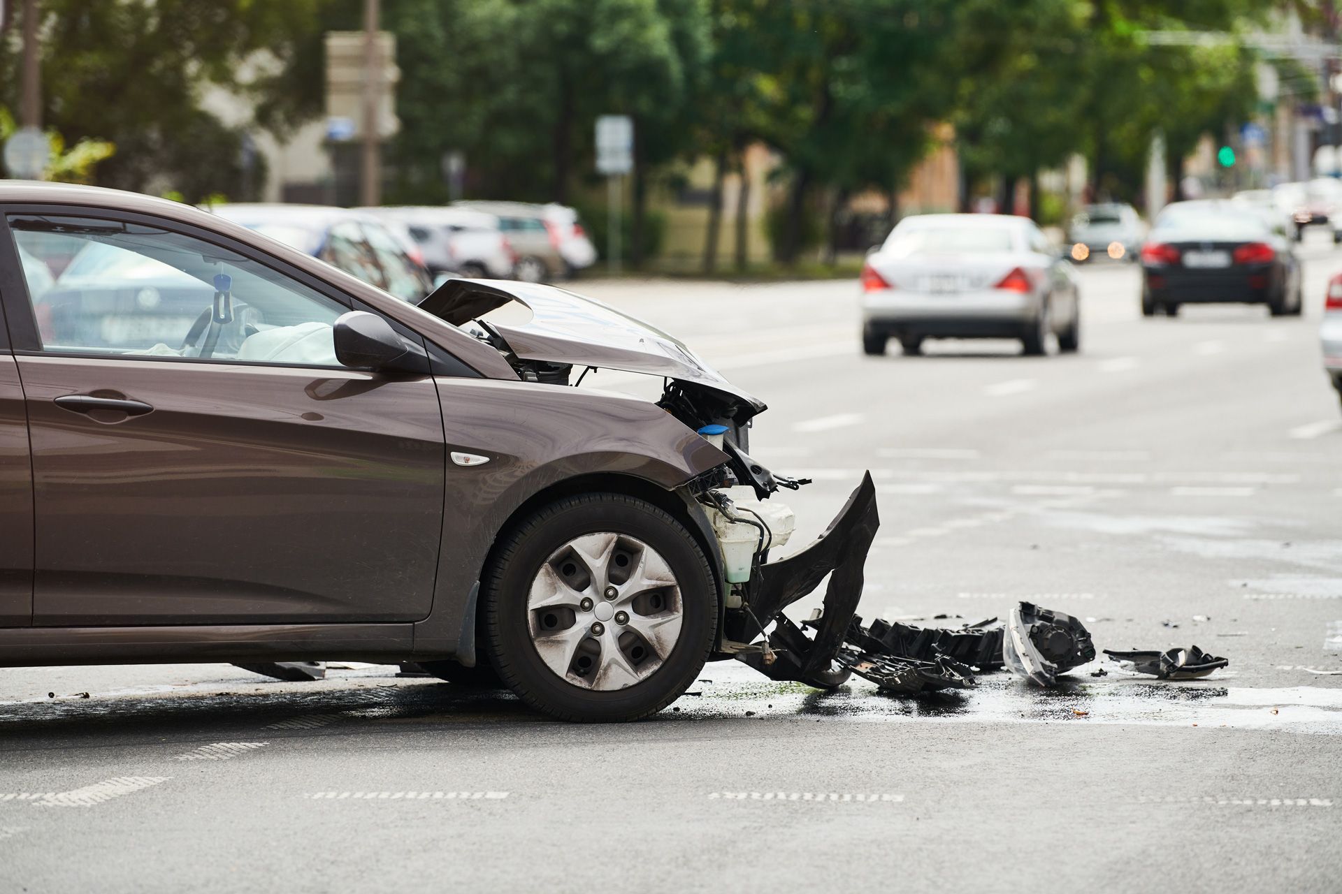 Damaged brown car at an intersection after a collision; debris and other vehicles visible.