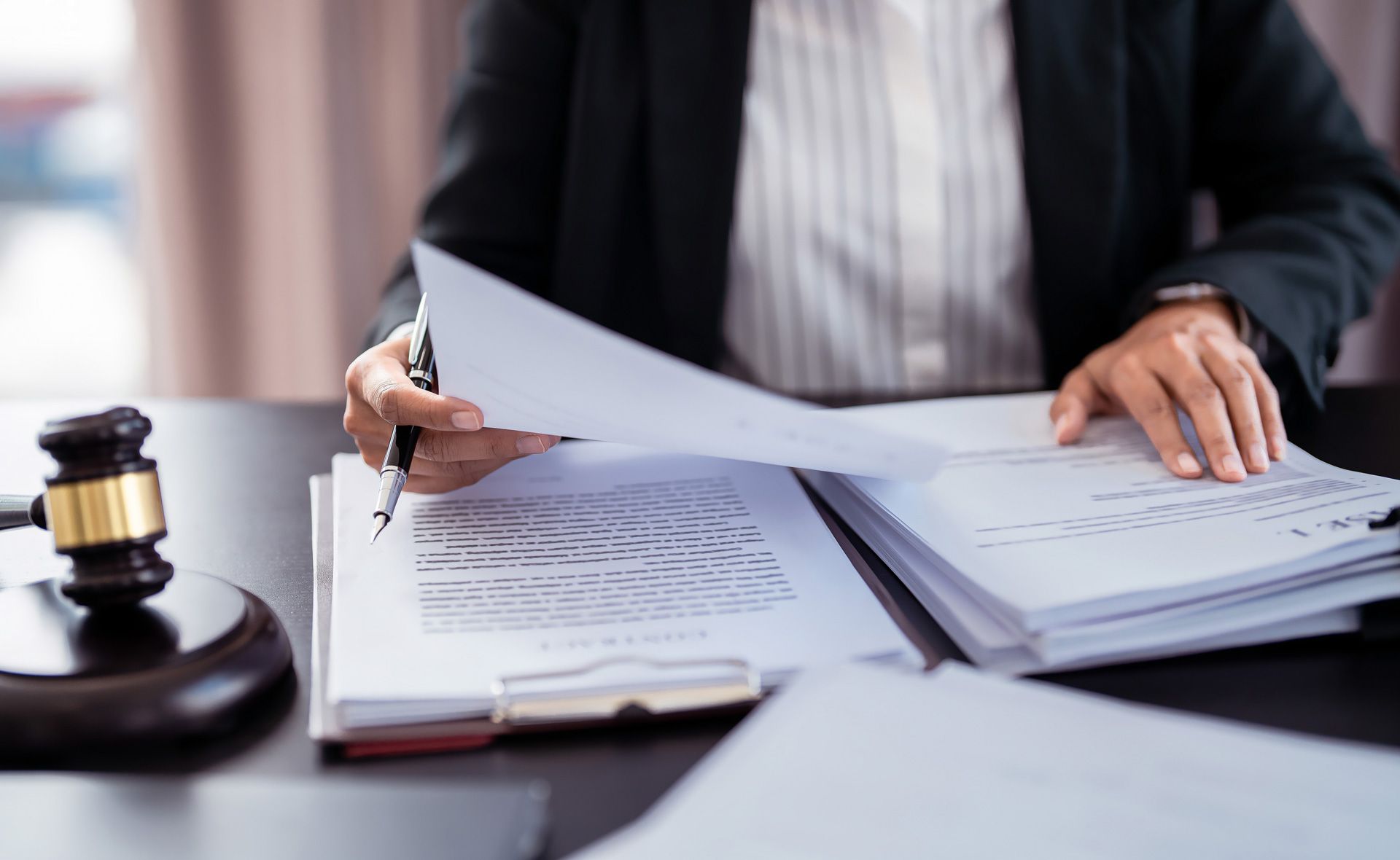 A person in a suit reviews documents on a desk with a gavel; indoors, professional setting.