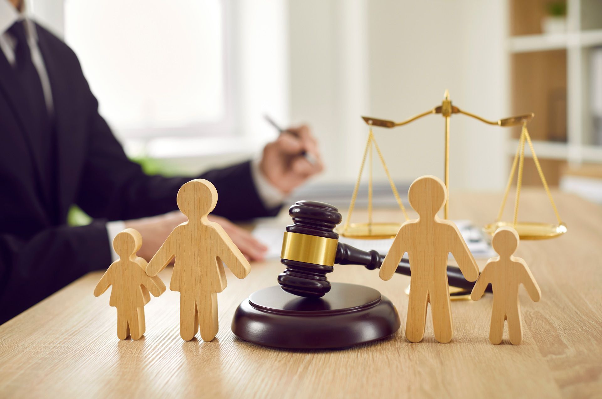 Lawyer with gavel and scales of justice, wooden family figures on desk.
