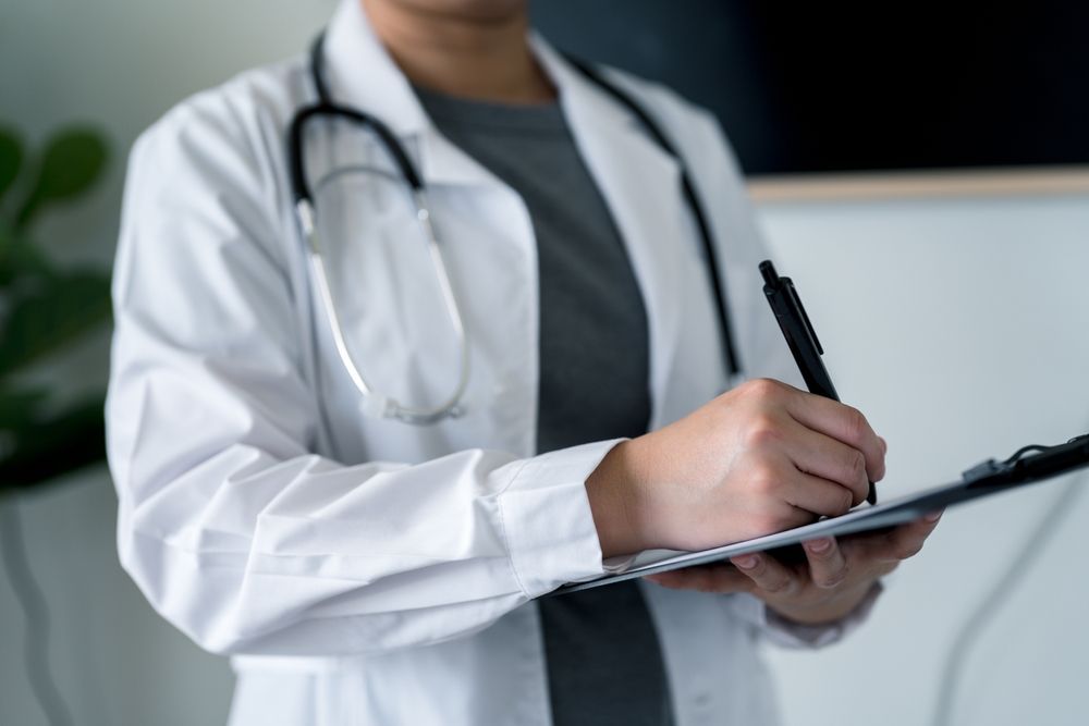 Doctor in white coat, stethoscope, taking notes on a clipboard.