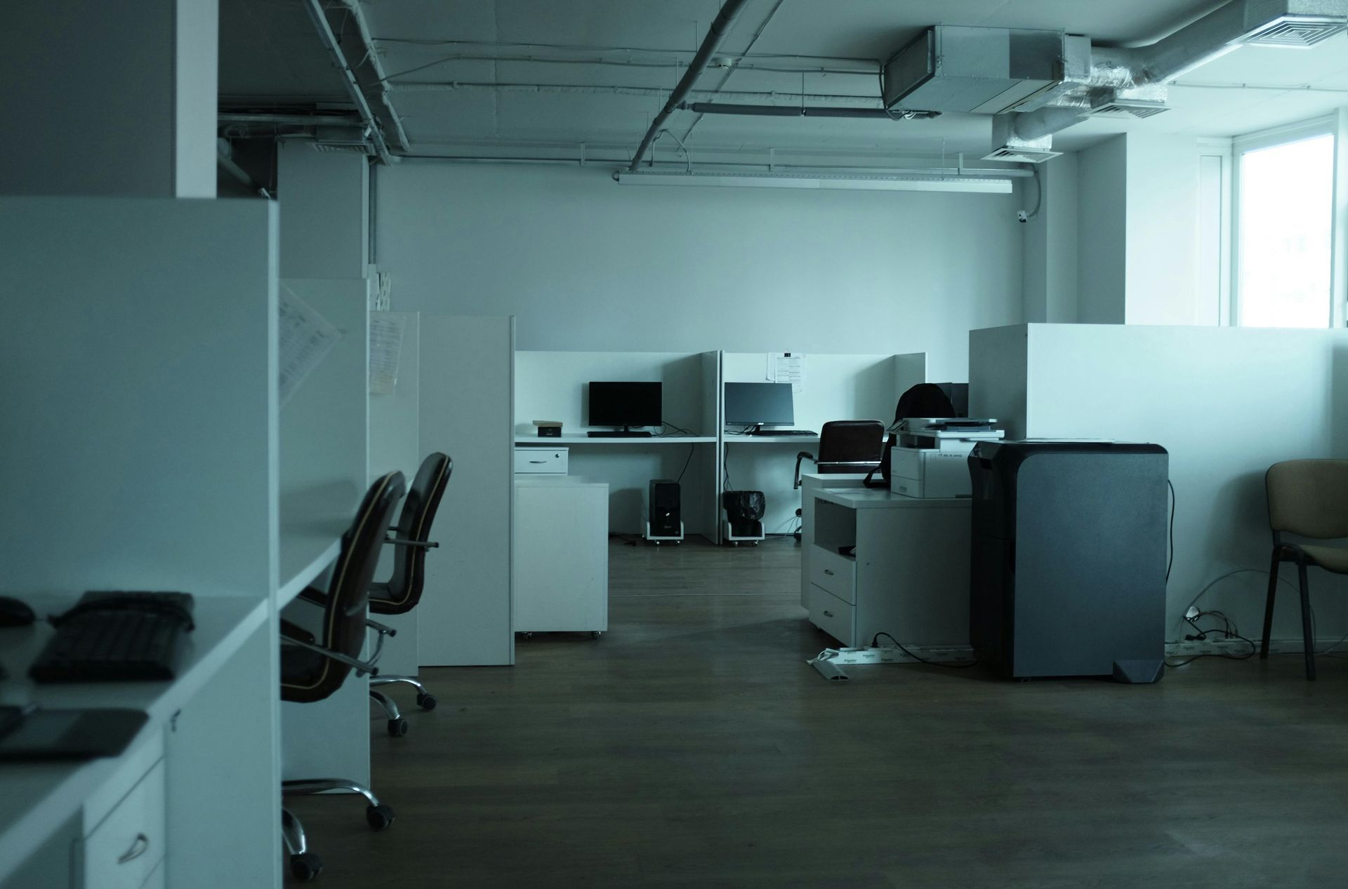 Modern open-plan office with desks, chairs, computers, and white partitions by large windows
