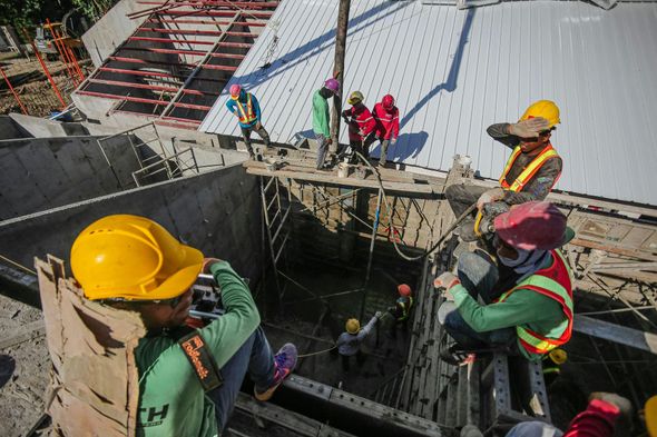 Construction workers in hard hats and safety vests work on a concrete building site, overseen by a supervisor.