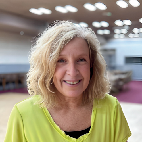 Woman with blonde hair wearing a bright green shirt smiles in a large room.