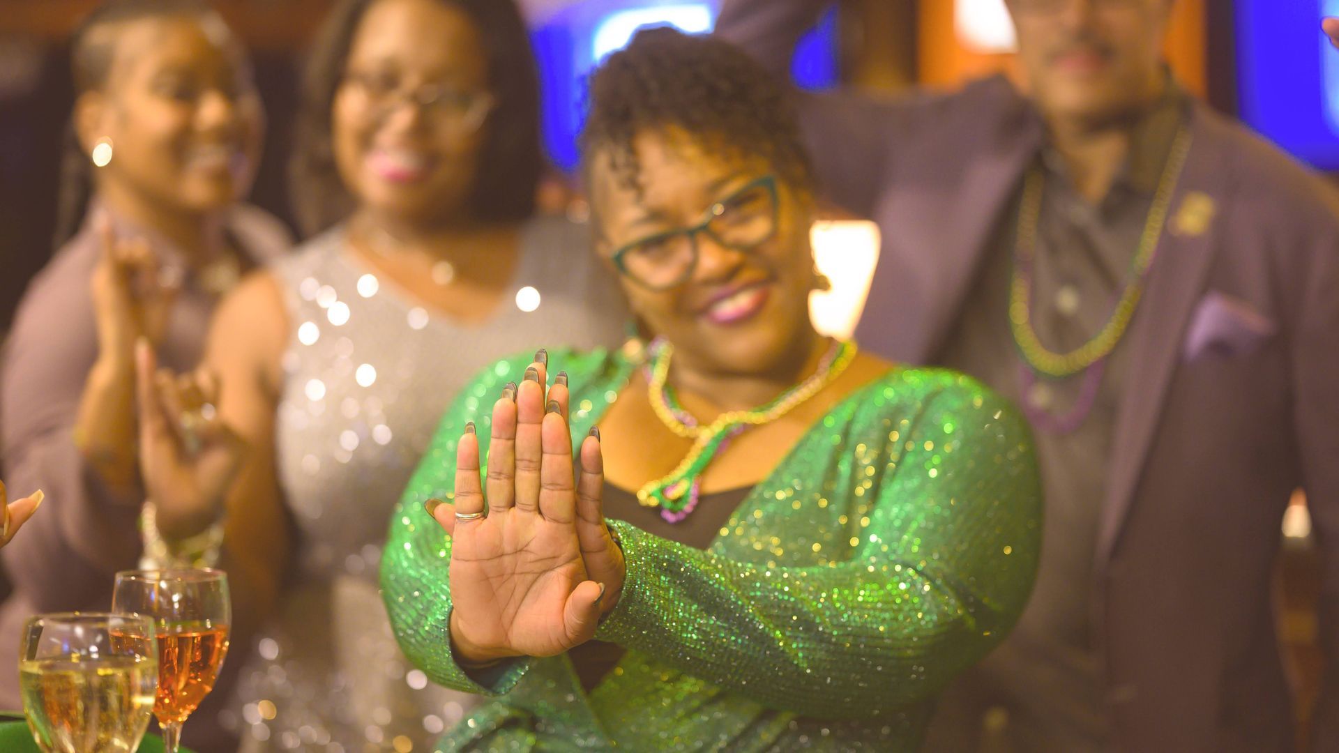 A woman in a green dress is standing in front of a group of people applauding.
