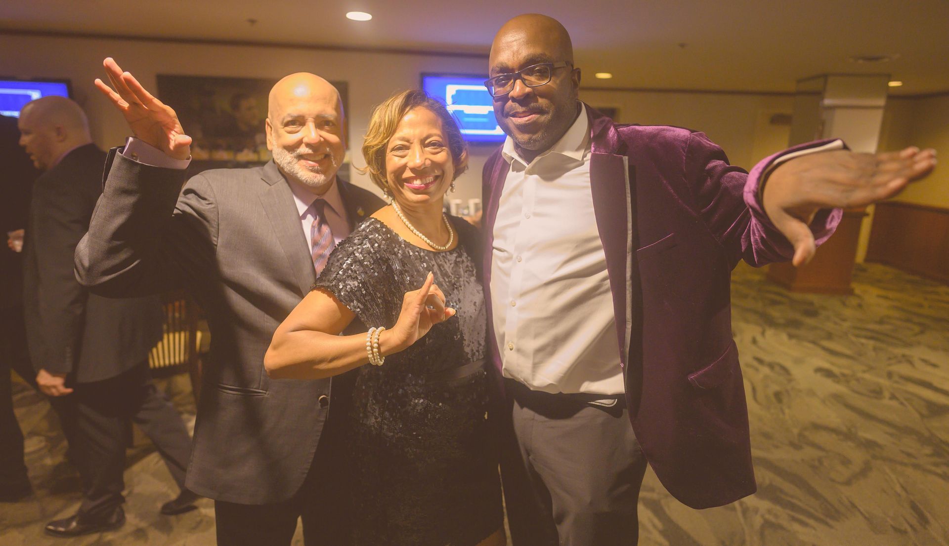 A man in a purple jacket is standing next to a woman and a man in a suit.