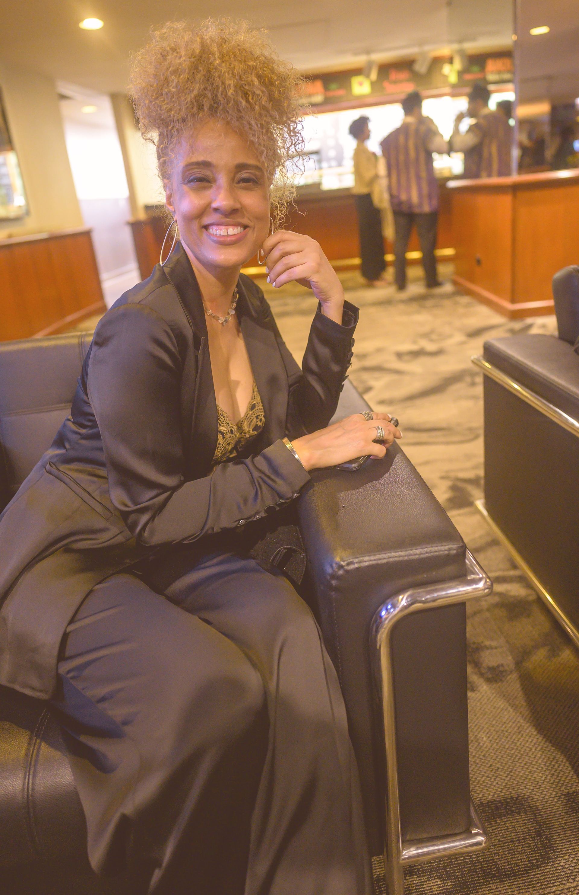 A woman in a black dress is sitting in a chair and smiling.