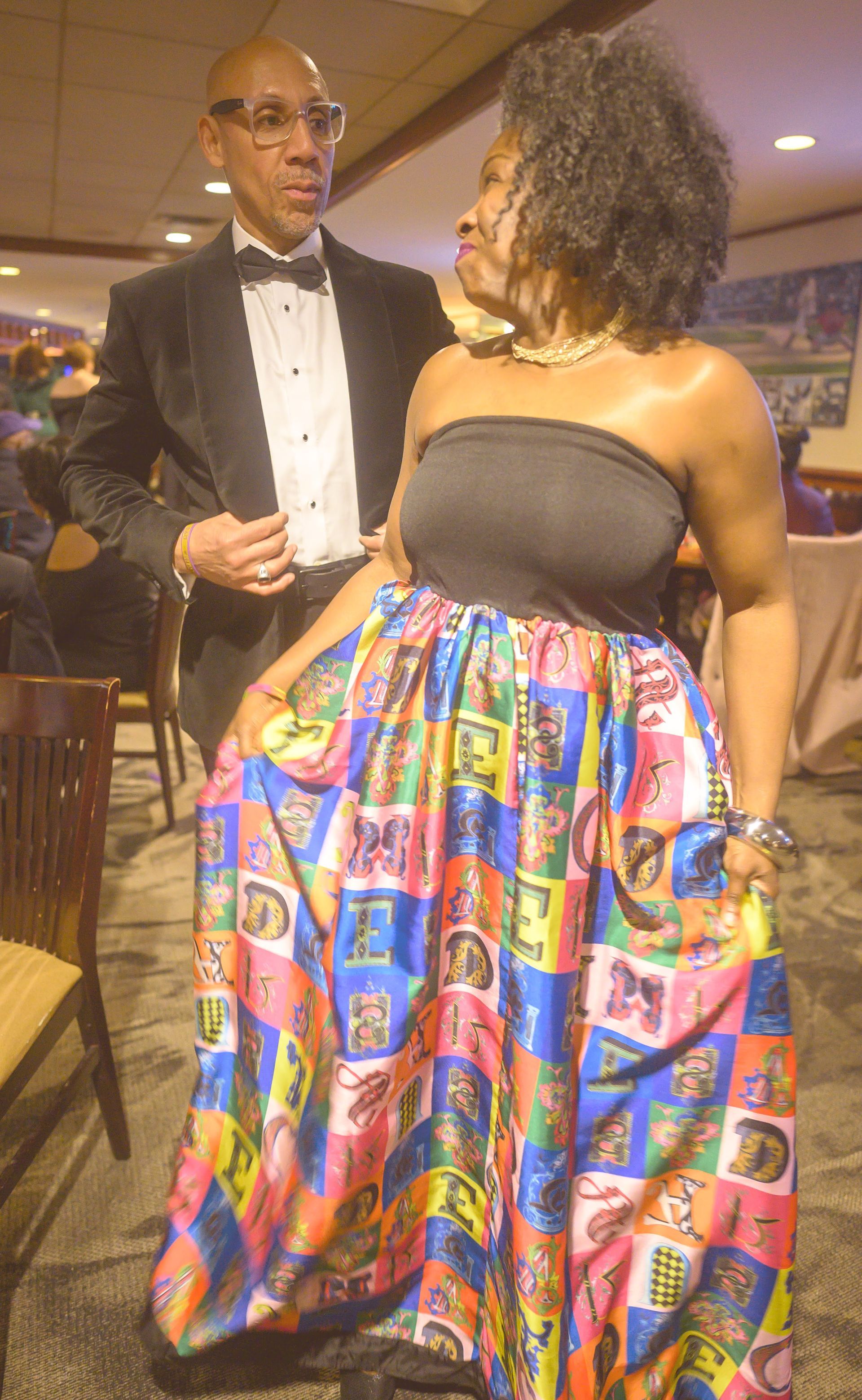 A woman in a colorful dress is standing next to a man in a tuxedo.