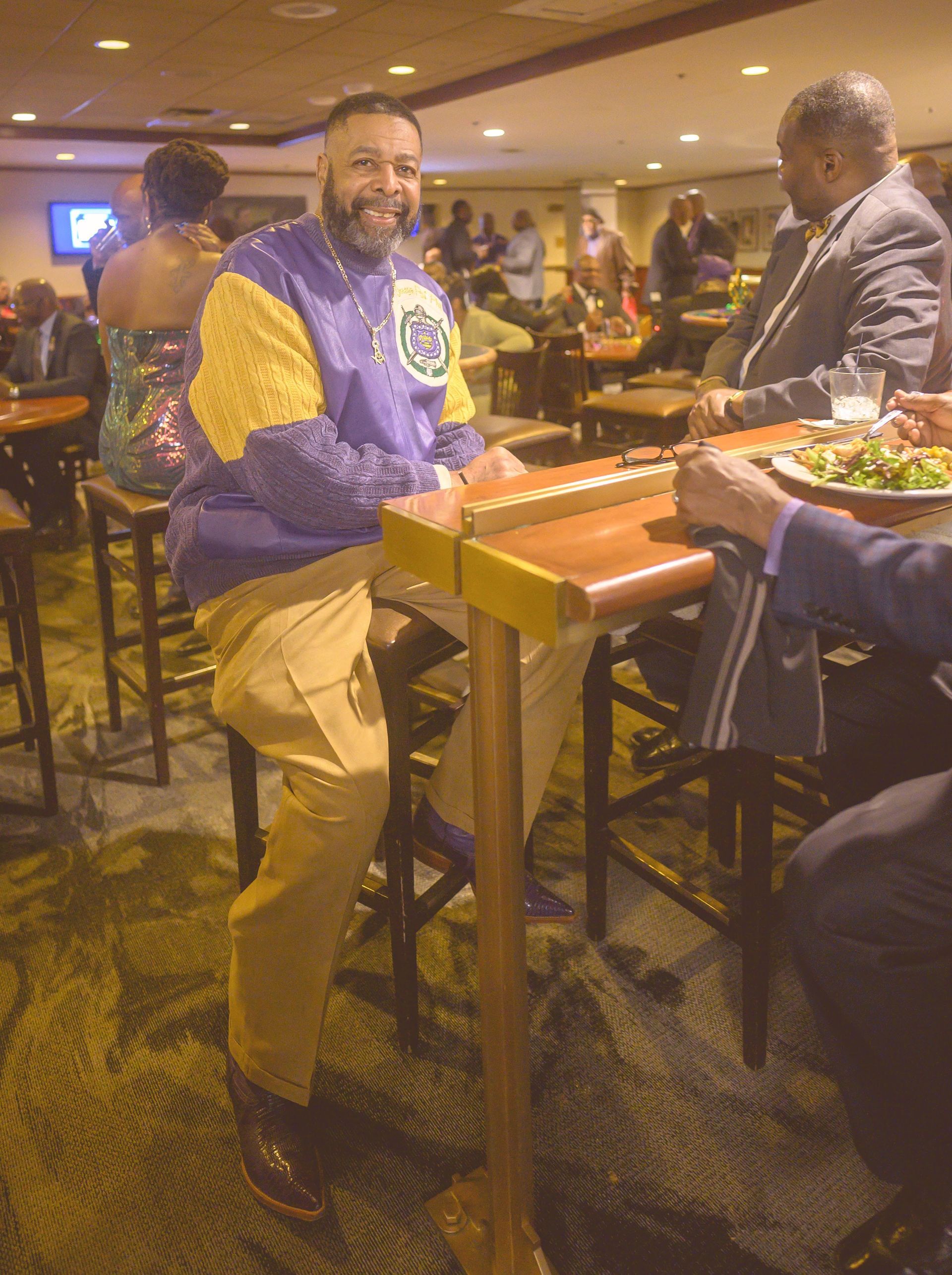 A man in a purple jacket is sitting at a table in a restaurant.