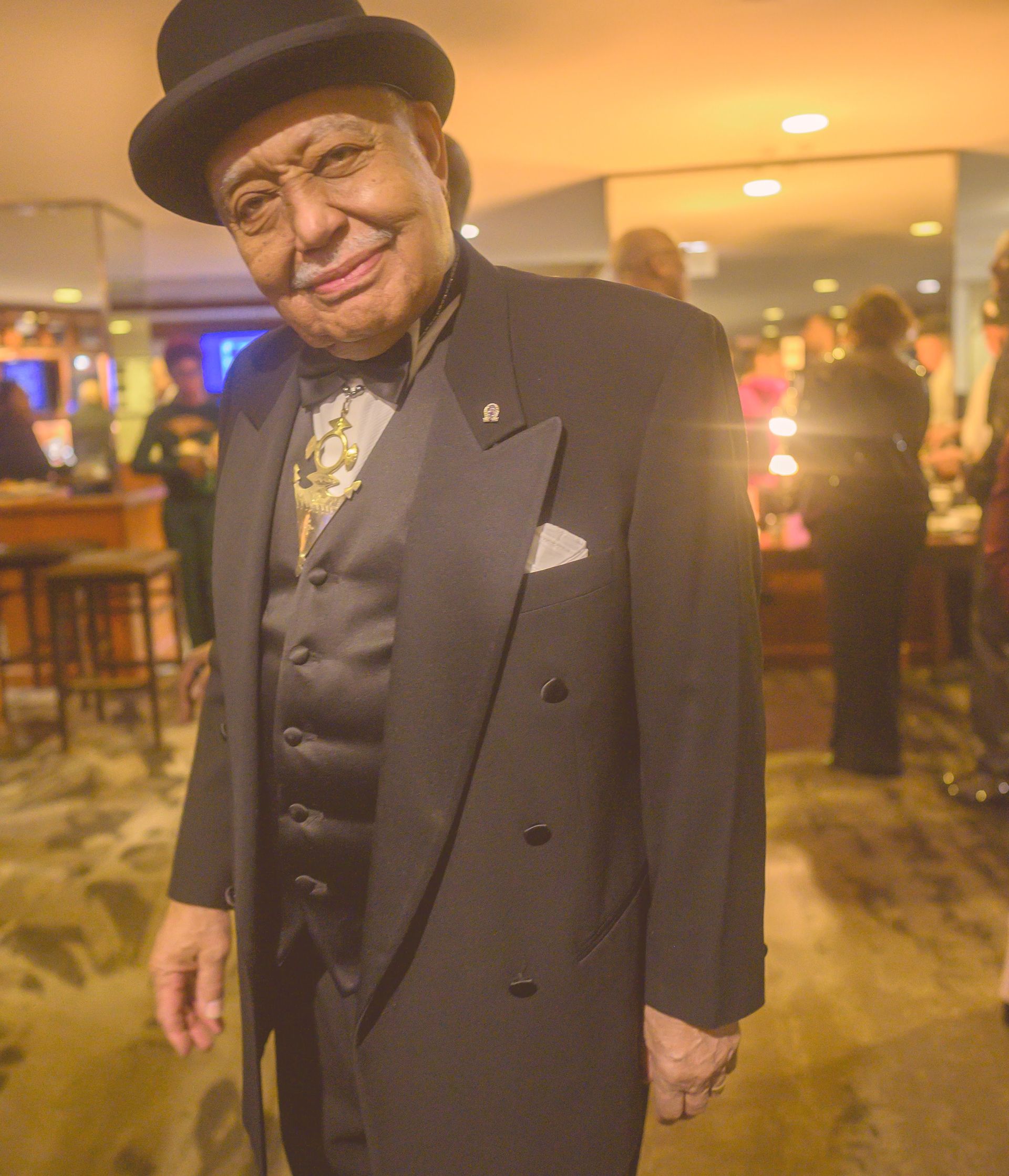 A man in a tuxedo and top hat smiles for the camera