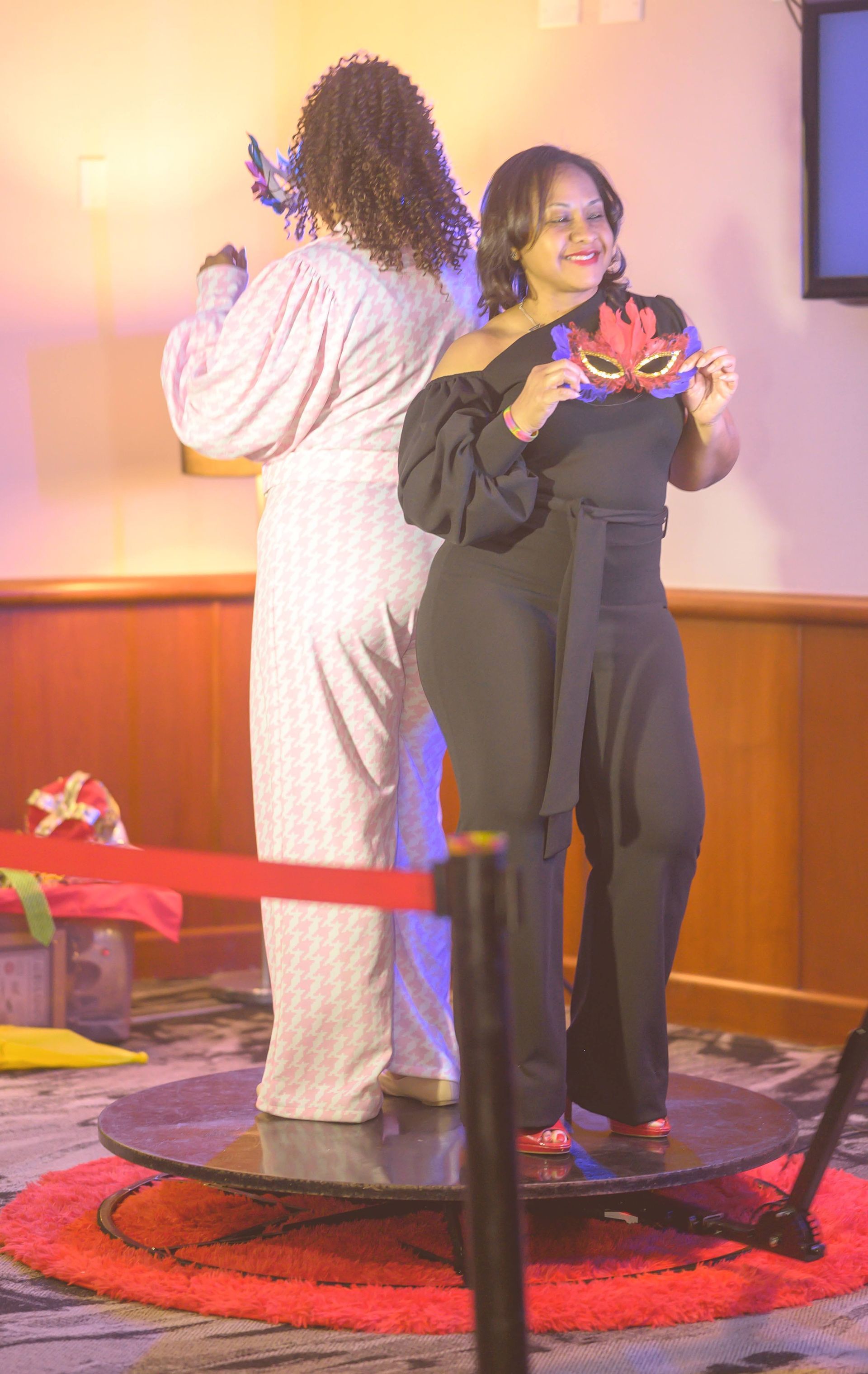 Two women are standing on a round table holding masks.