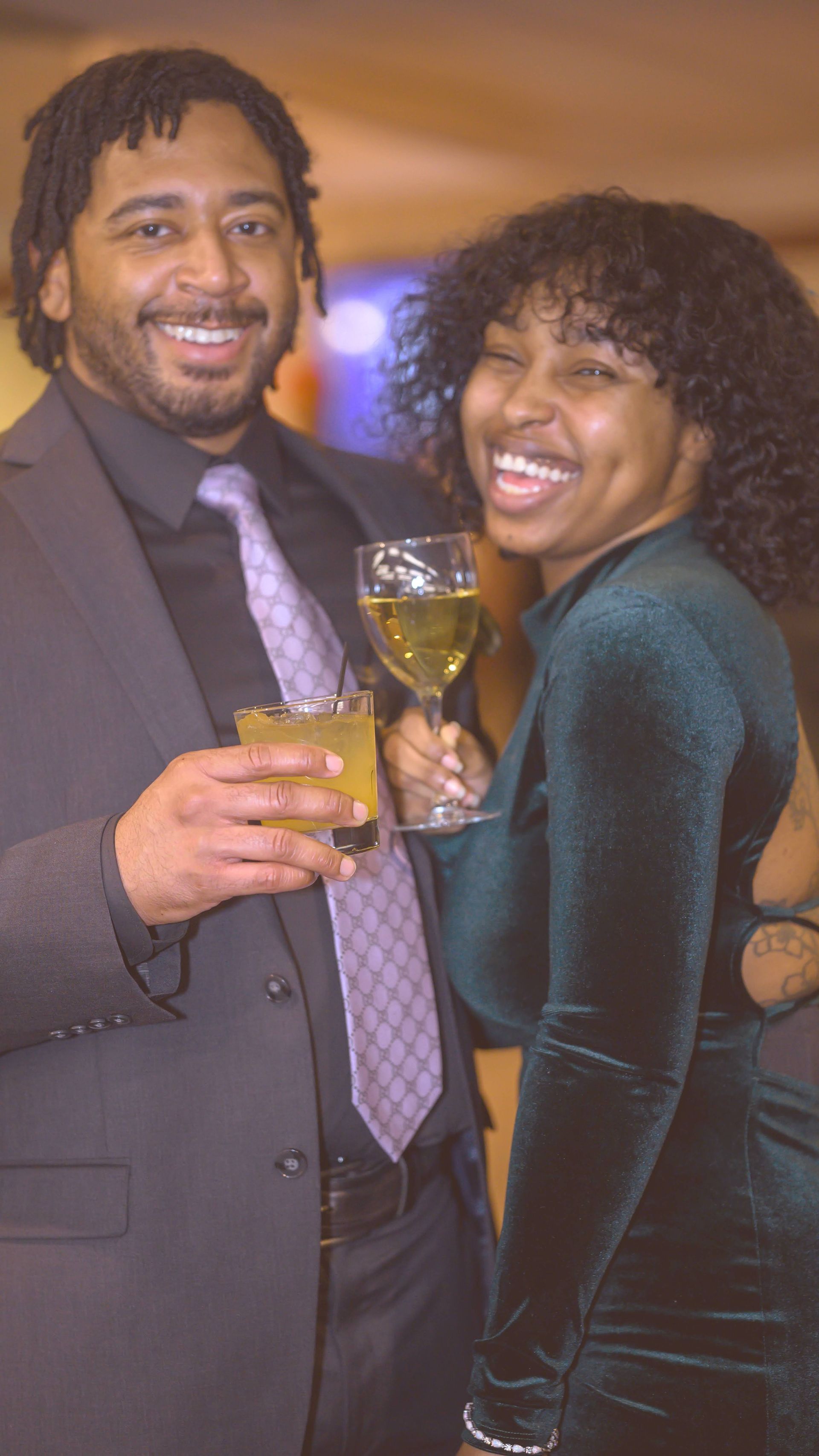 A man in a suit and tie is holding a glass of wine next to a woman in a green dress.