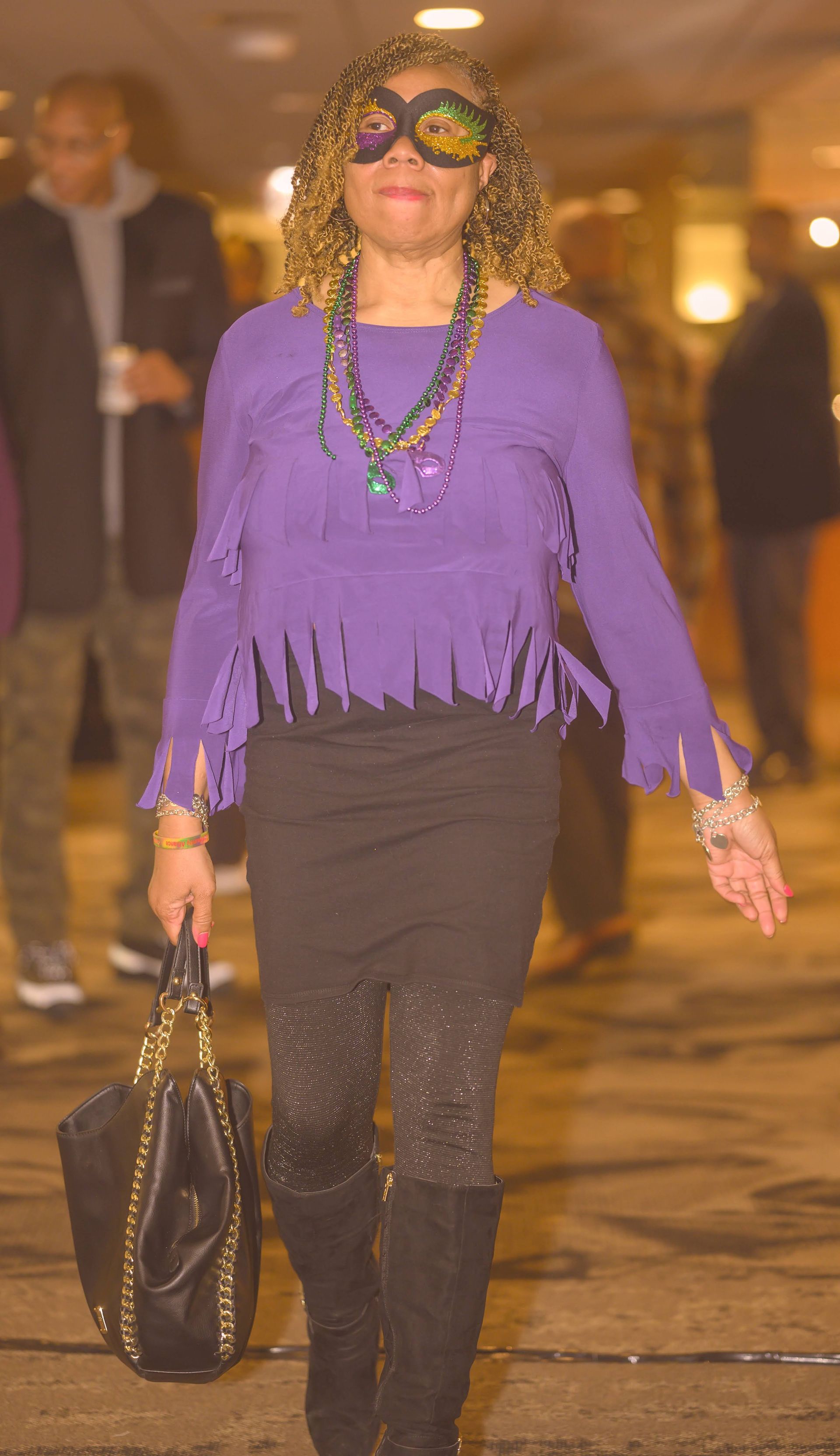 A woman wearing a mask and a purple top is walking down a hallway.
