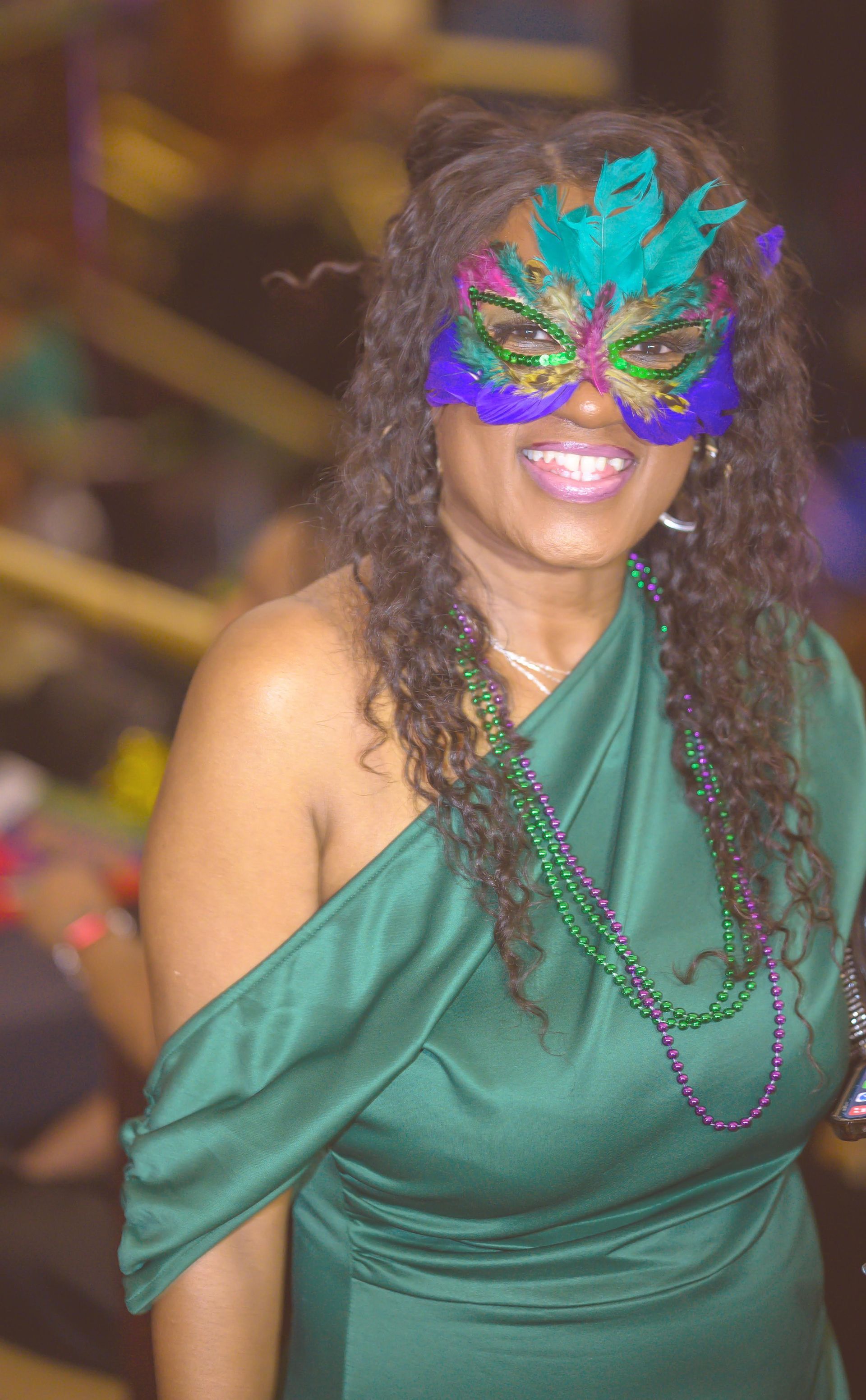 A woman in a green dress is wearing a mardi gras mask.
