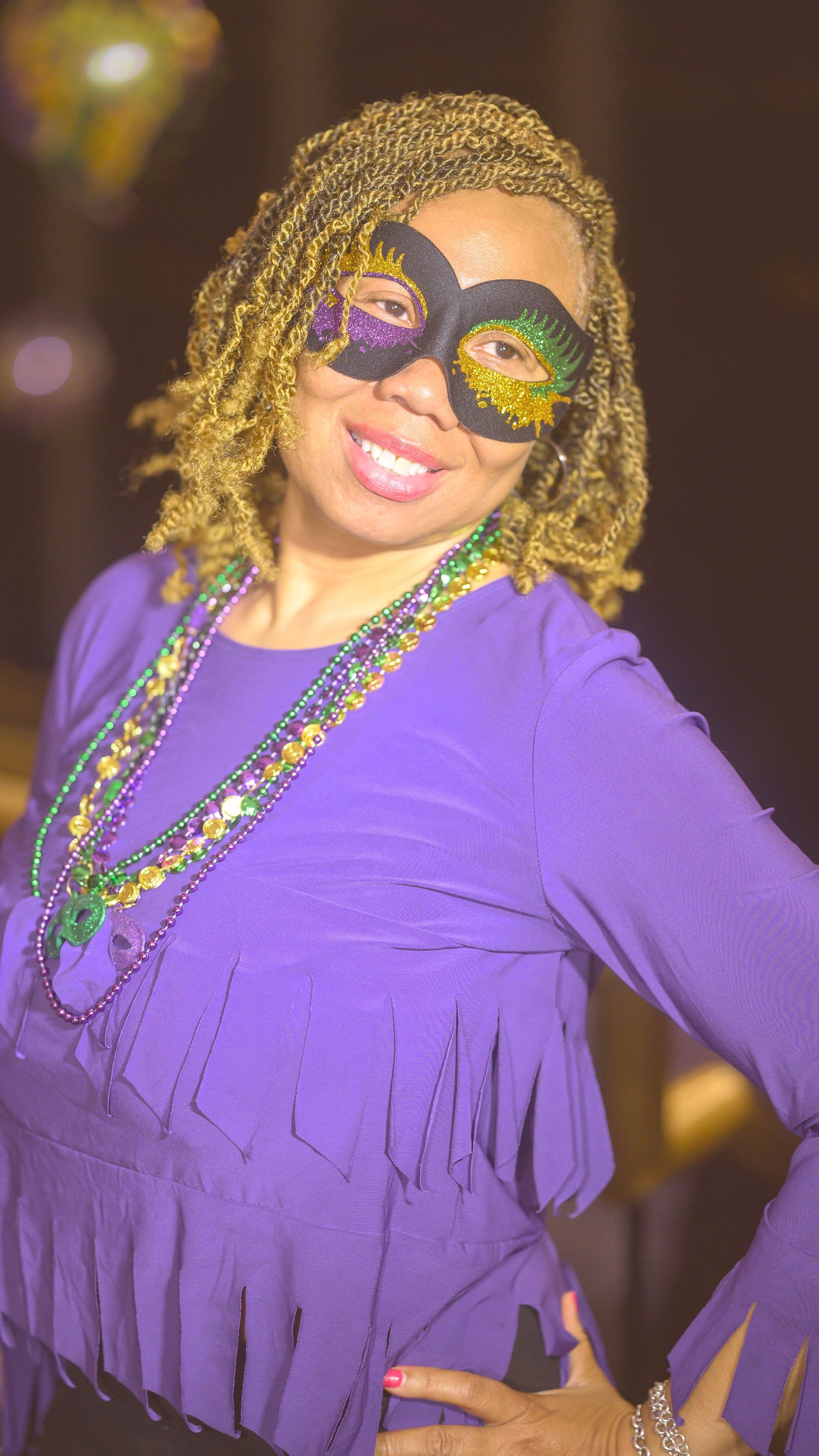 A woman is wearing a mardi gras mask and a purple dress.