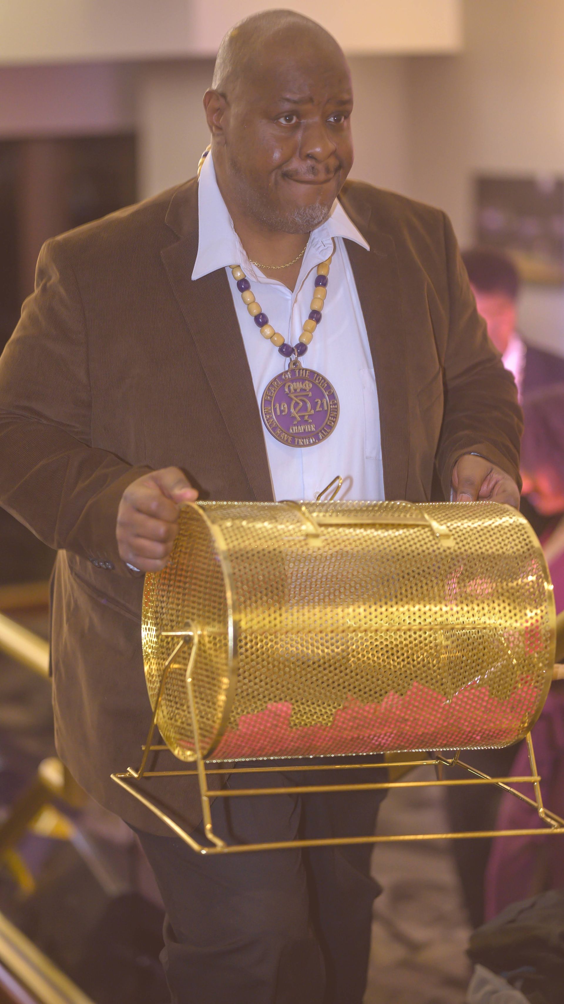 A man in a suit is holding a gold barrel filled with red balls.