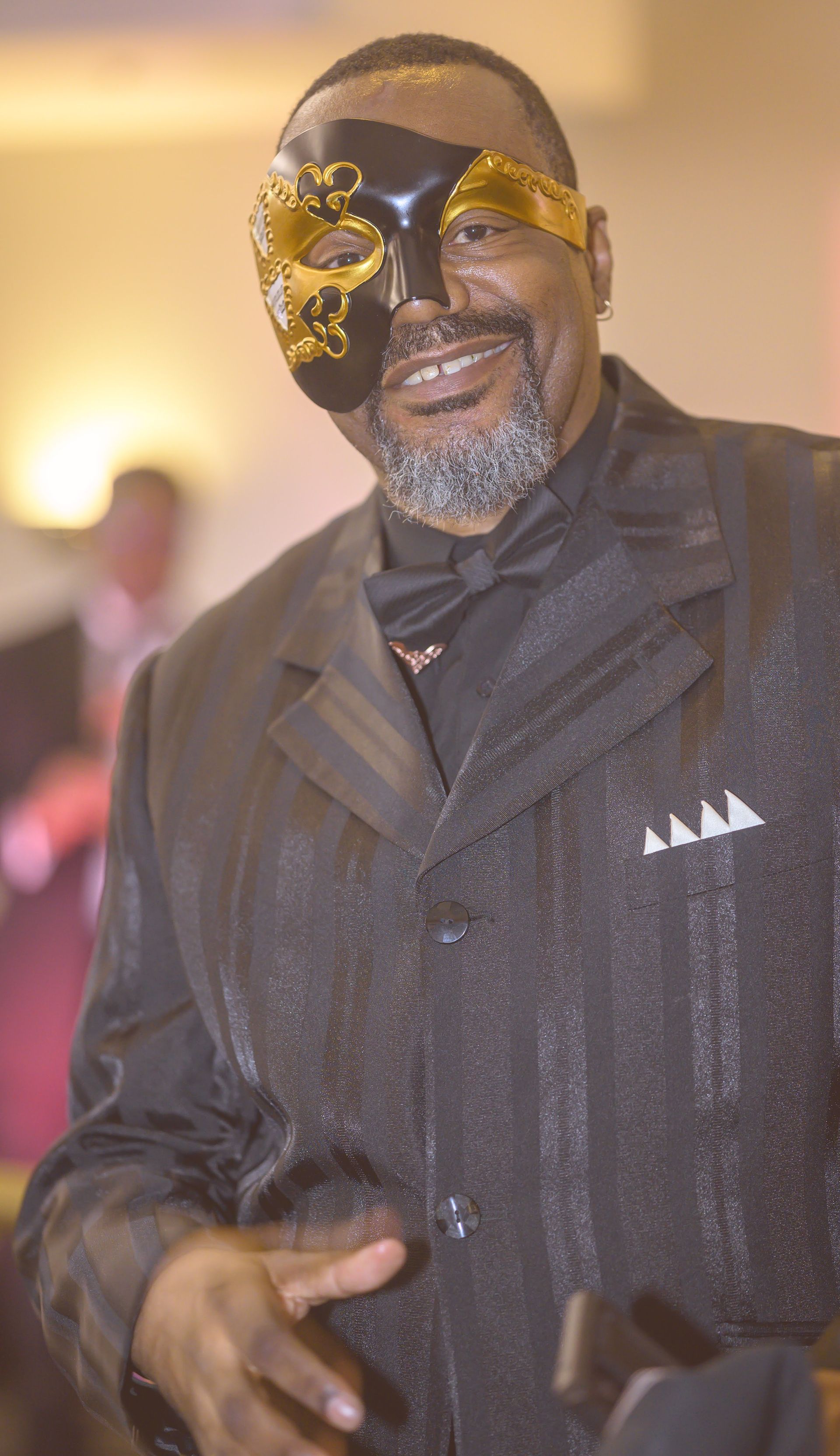 A man wearing a mask and a suit is holding a glass of wine.
