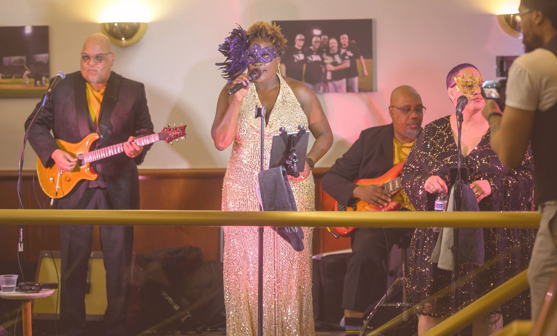 A woman in a mask is singing into a microphone while a man plays a guitar.