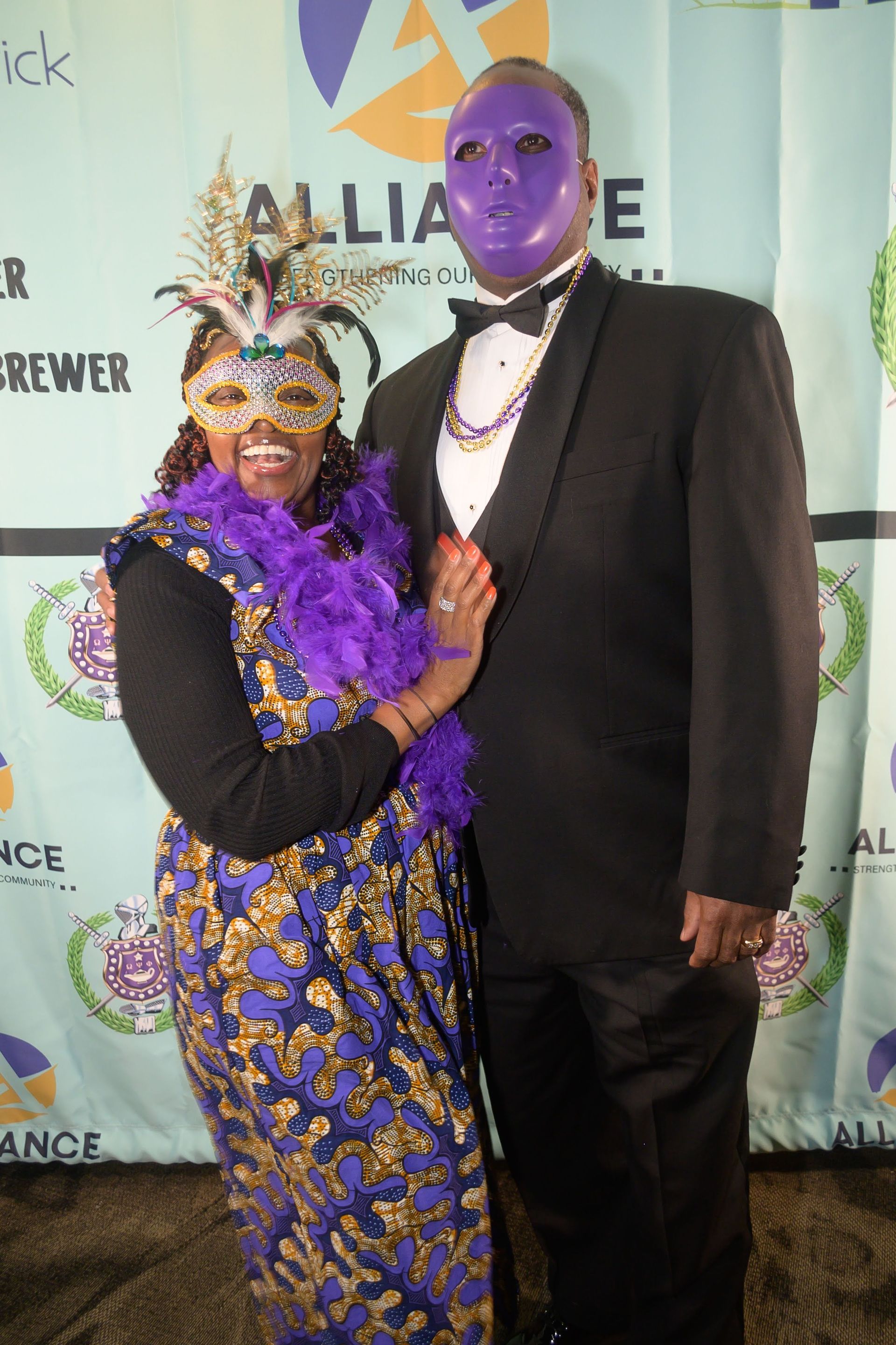 A man in a tuxedo and a woman in a purple mask pose for a picture