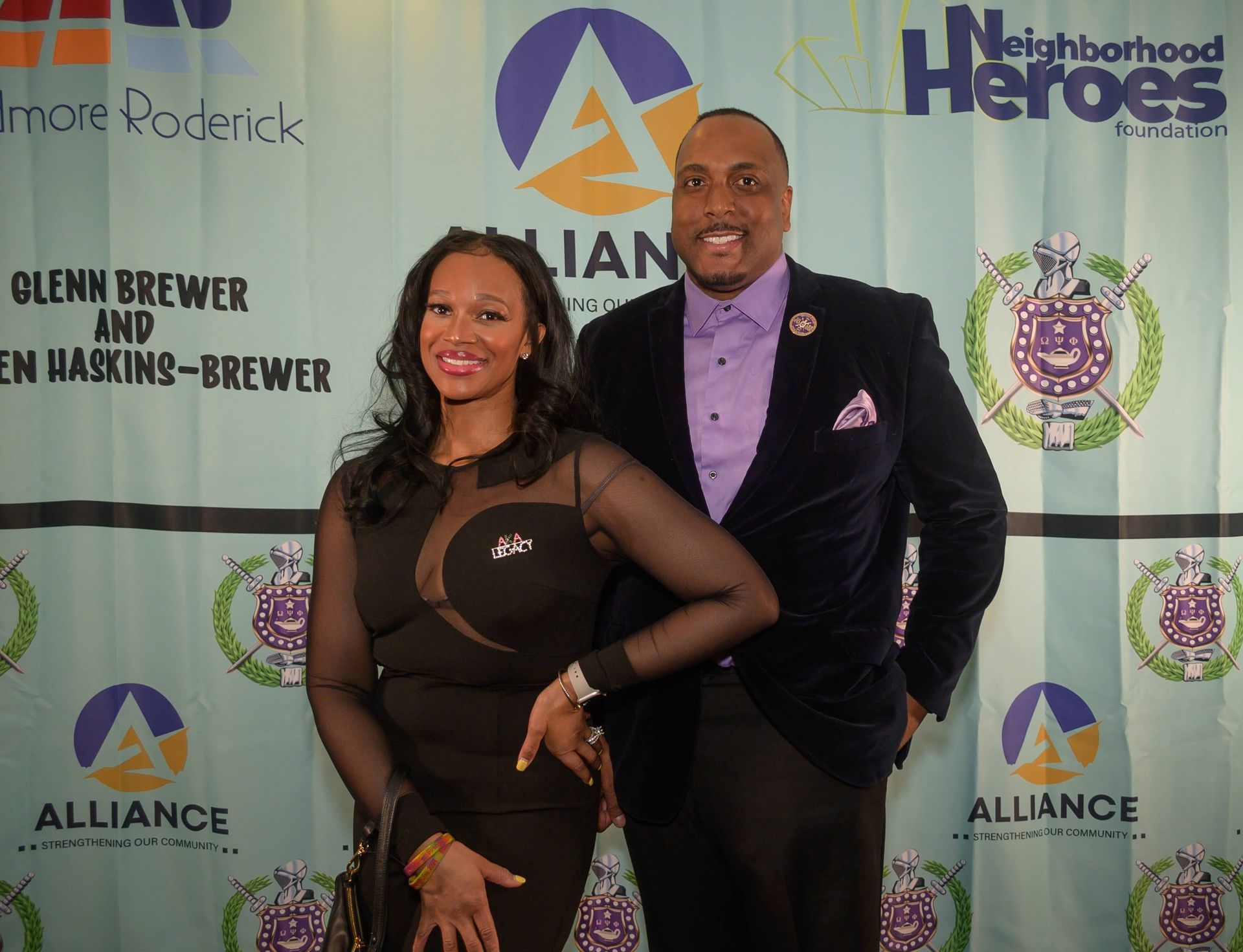 A man and a woman are posing in front of a backdrop that says neighborhood heroes