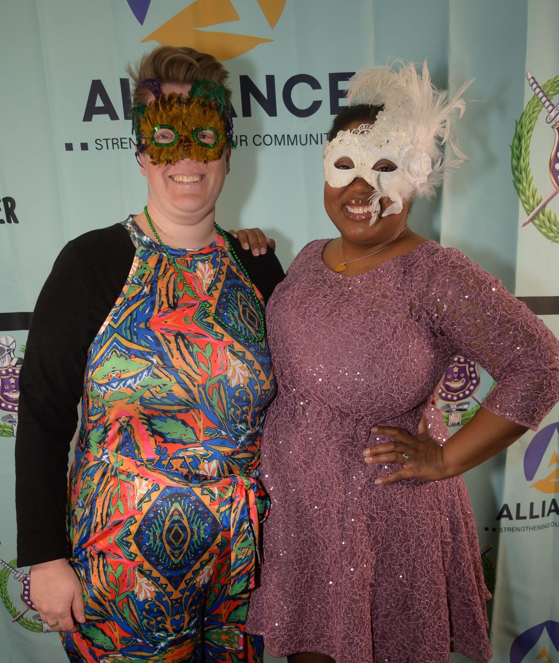 Two women wearing masks are posing for a picture in front of a banner that says alliance
