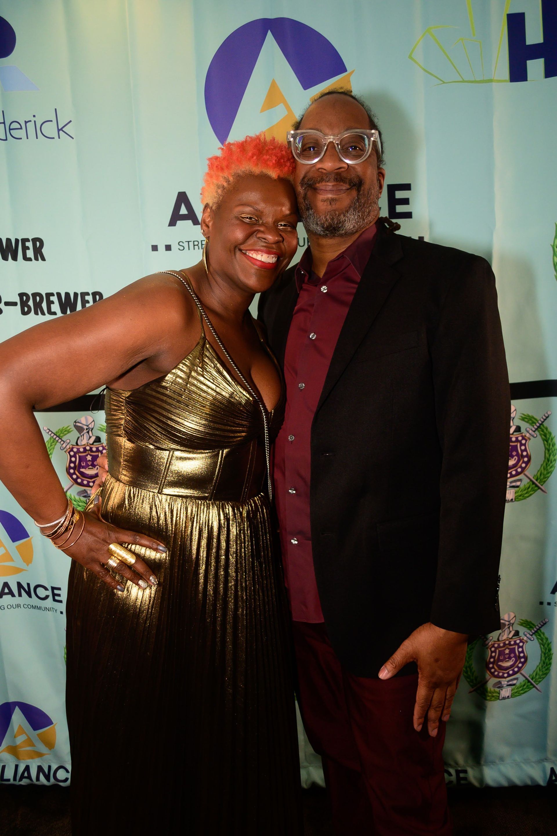 A man and a woman are posing for a picture in front of a backdrop.
