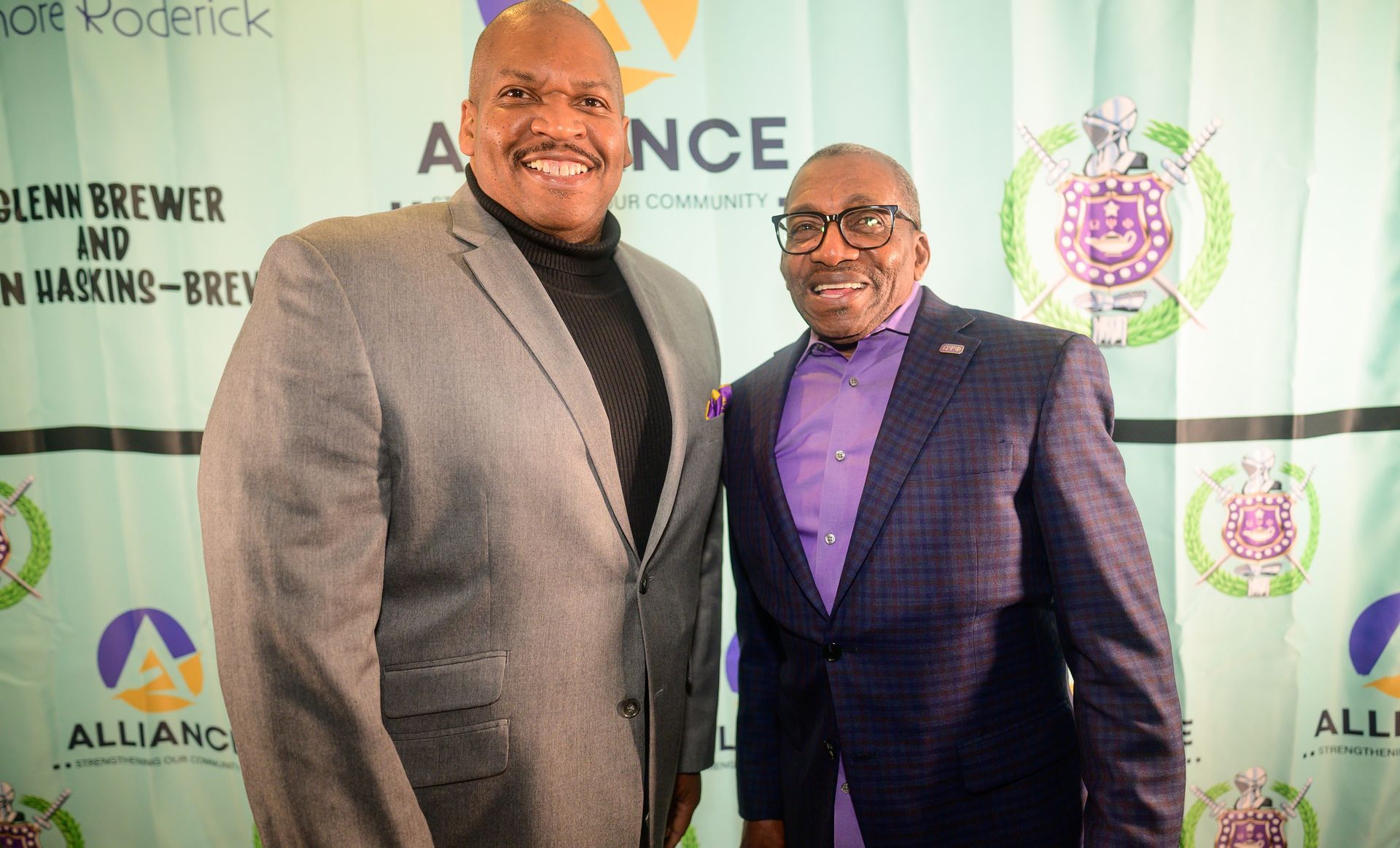 Two men in suits are standing next to each other in front of a wall.