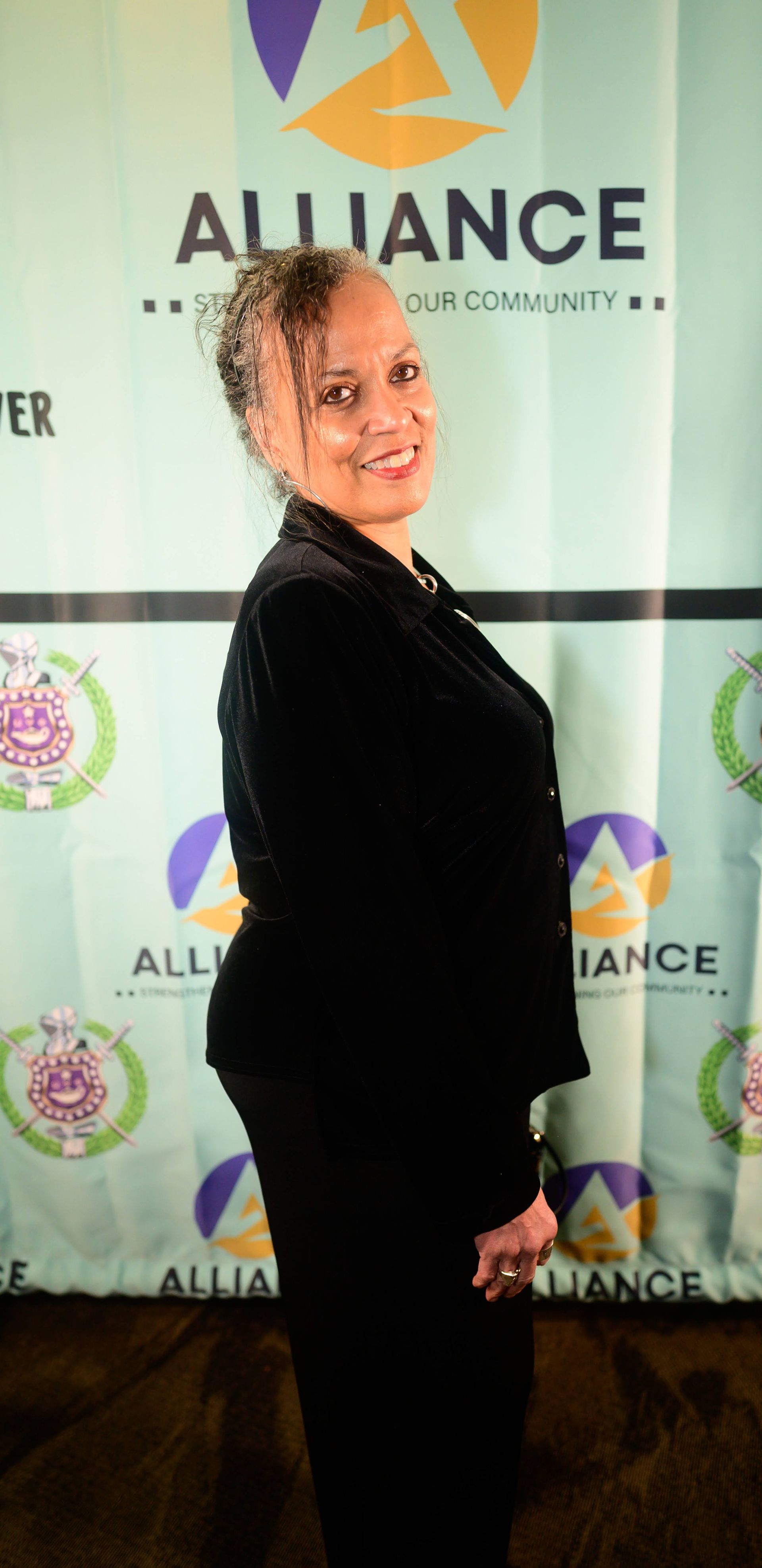 A woman in a black suit is standing in front of a alliance banner.
