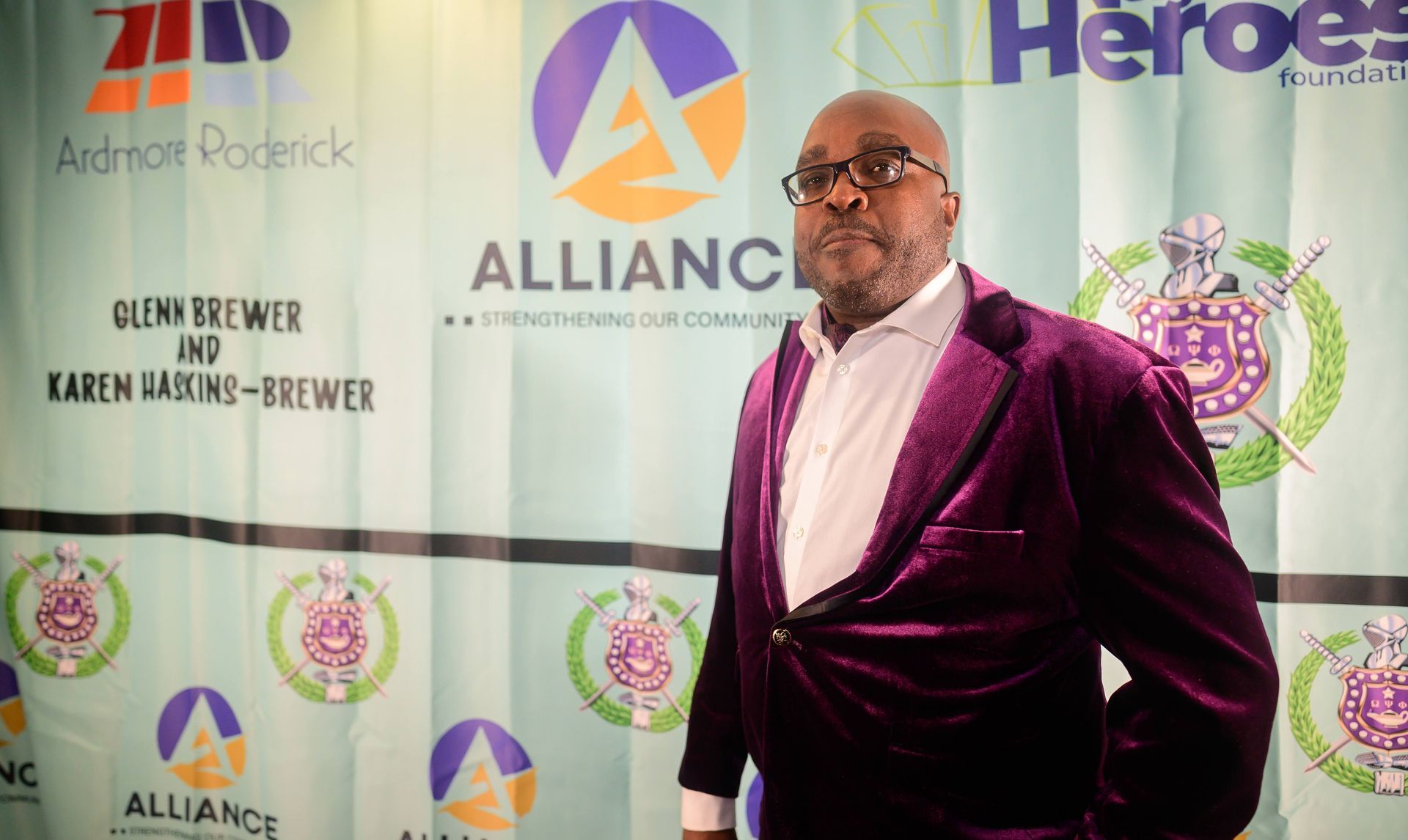A man in a purple suit is standing in front of a banner that says alliance heroes.