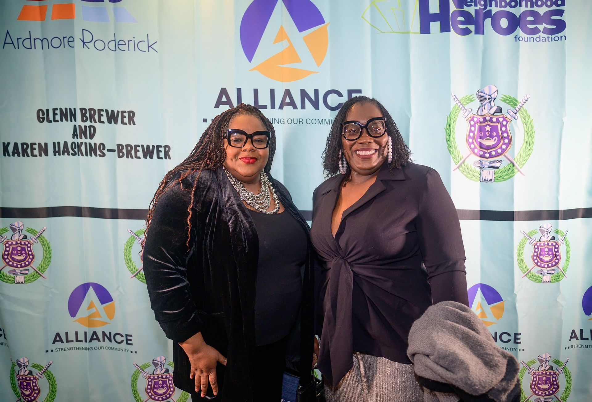 Two women are posing for a picture in front of a alliance banner.