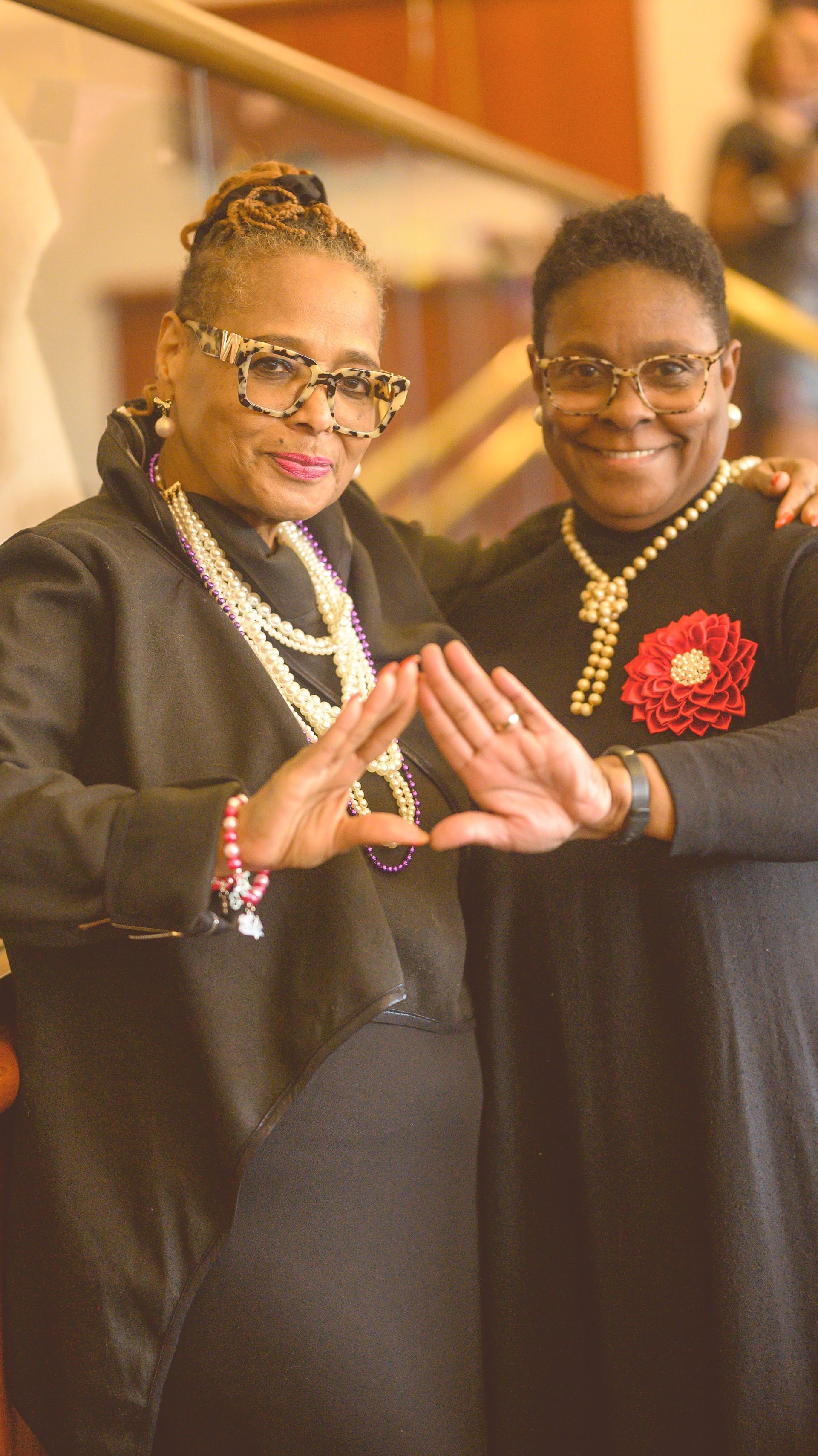 Two women are standing next to each other and making a triangle with their hands.
