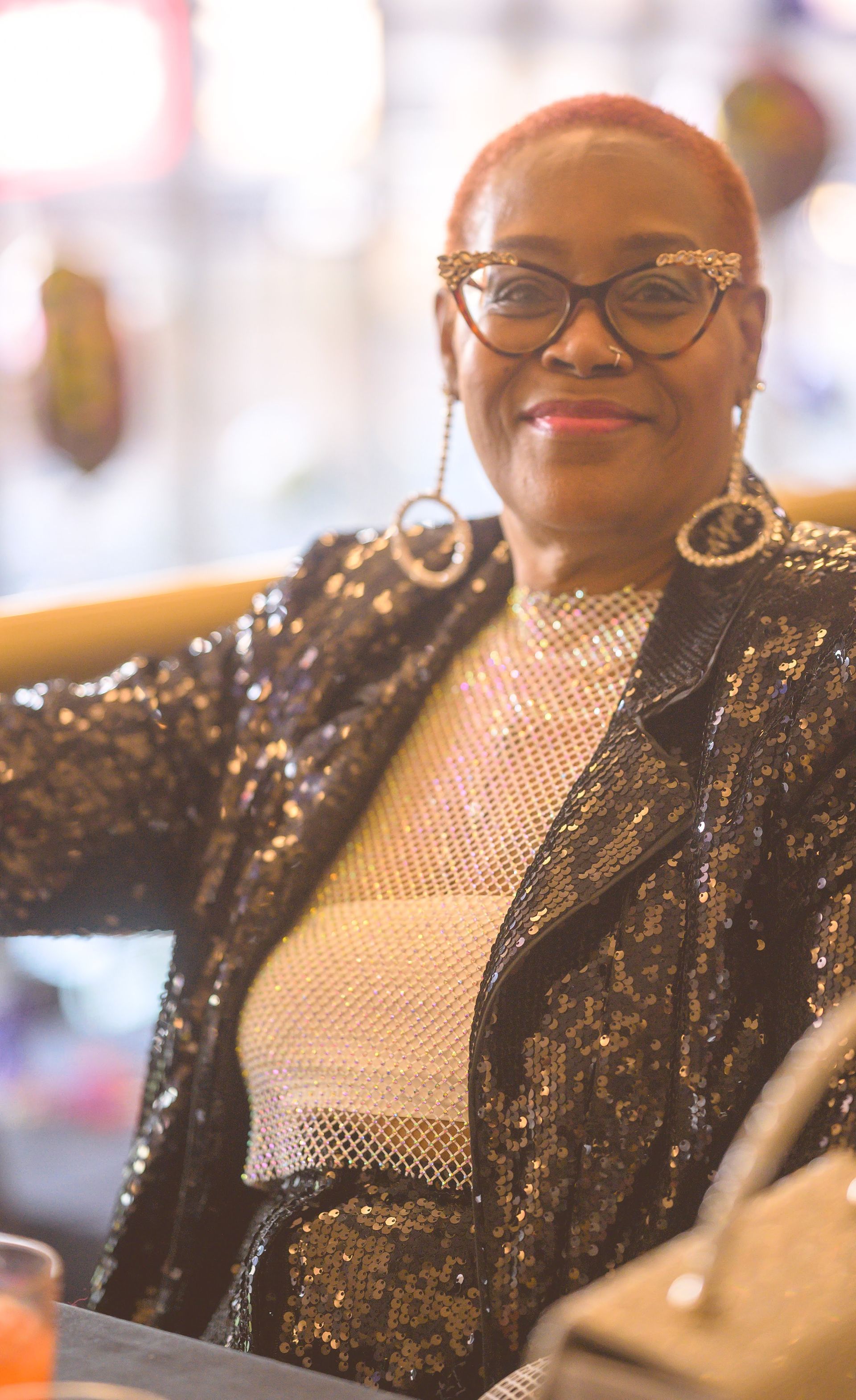 A woman wearing glasses and a sequined jacket is sitting at a table.