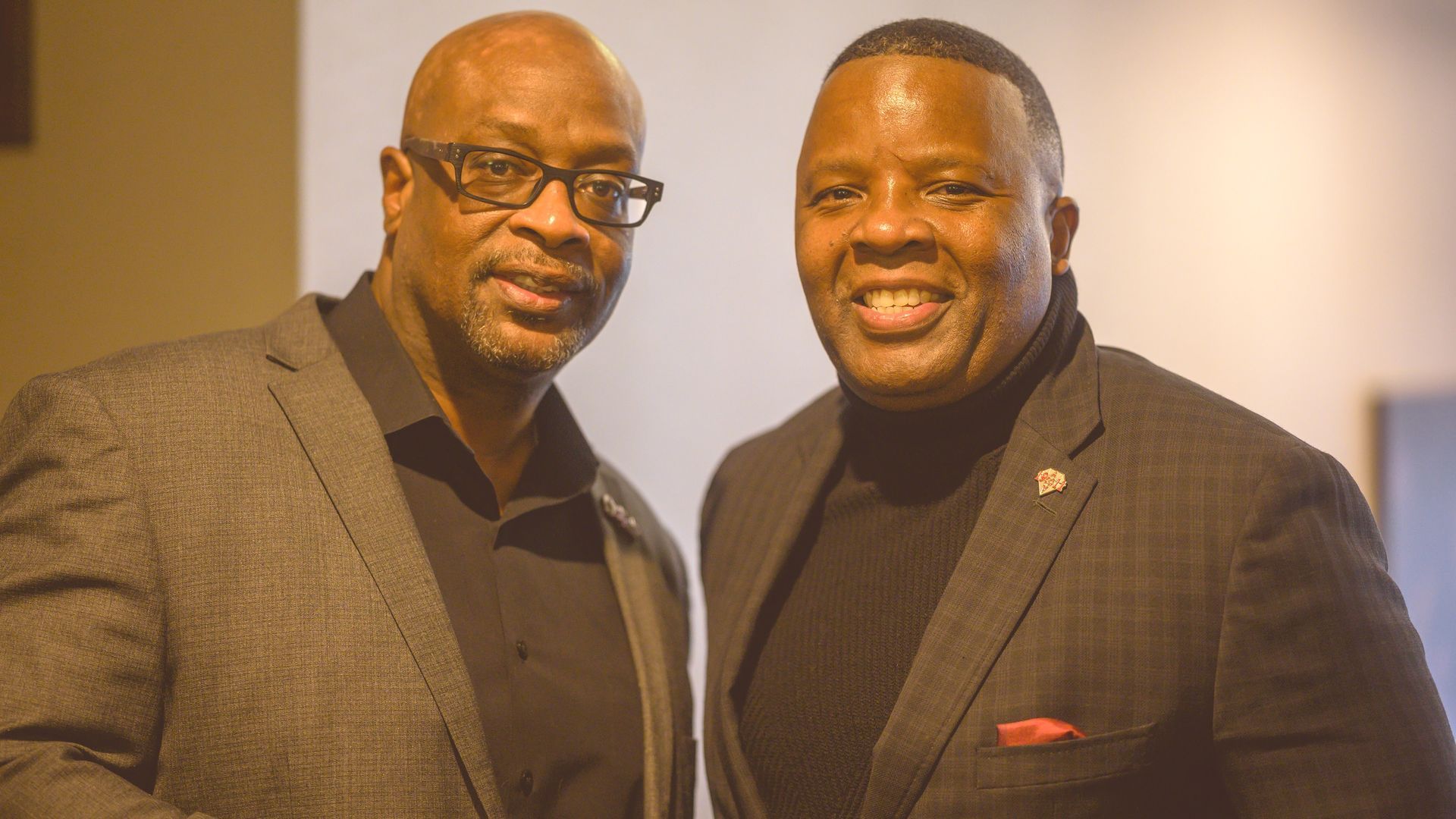 Two men in suits and glasses are posing for a picture.
