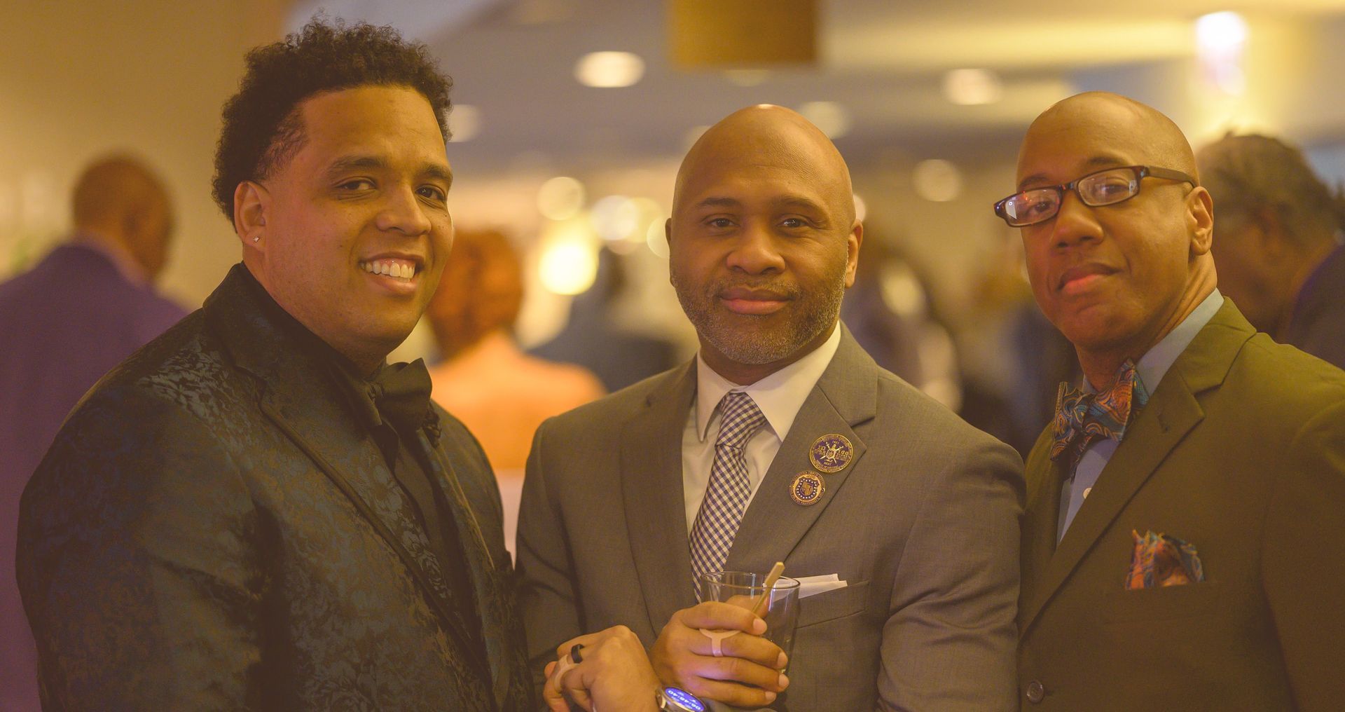 Three men in suits and ties are posing for a picture at a party.