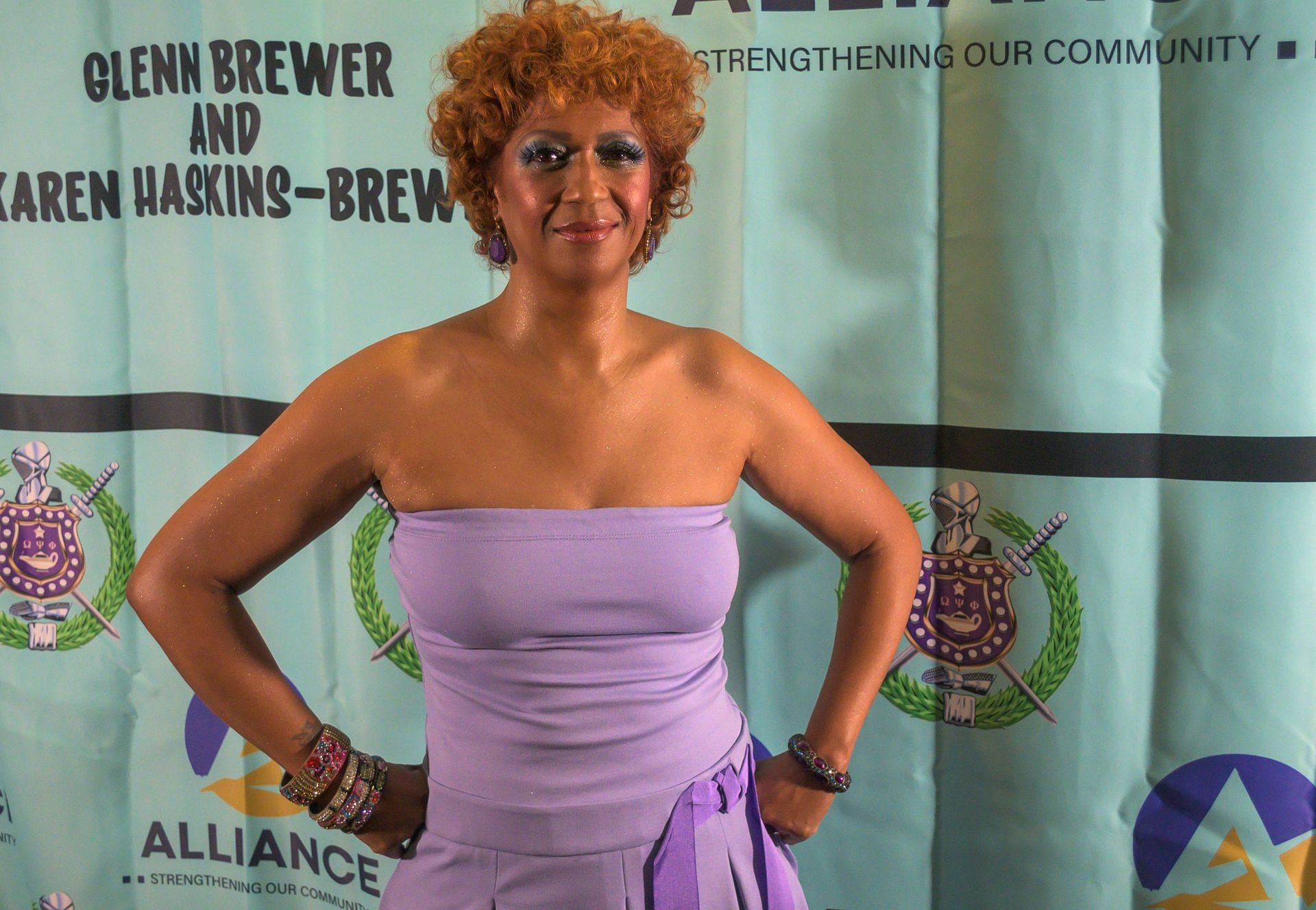 A woman in a purple dress stands in front of a sign that says alliance