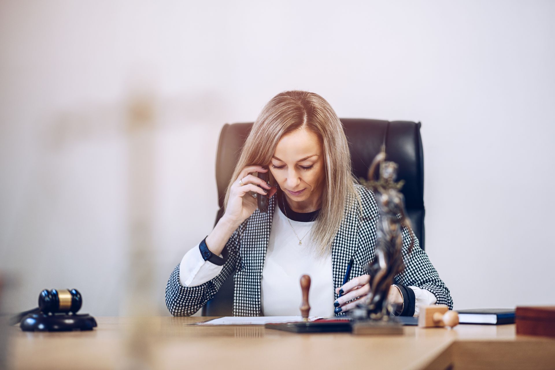 A professional at a desk with a gavel and scales of justice, speaking on a phone while reviewing documents.