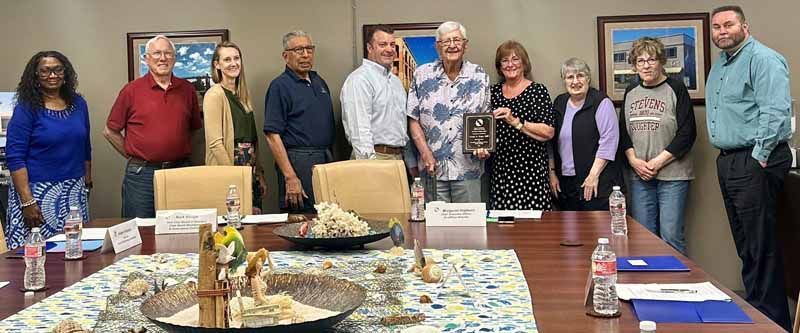 Group of people around a table, holding an award. Inside a room, with artwork on the wall.