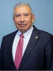 Man in dark suit with pink tie, smiling.