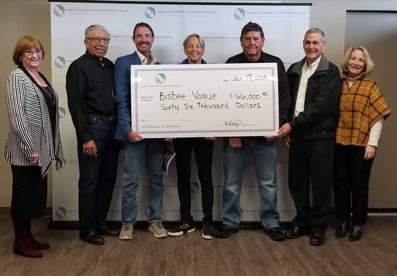 Group of people holding large check; indoors, celebratory smiles.