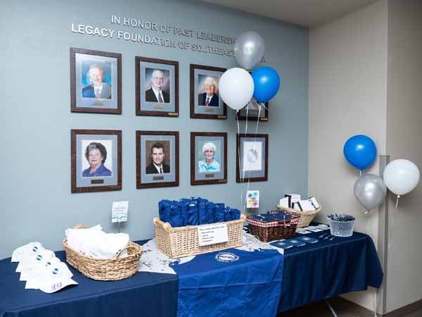 Celebration with framed portraits, blue and silver balloons, and a table with gifts and decorations.