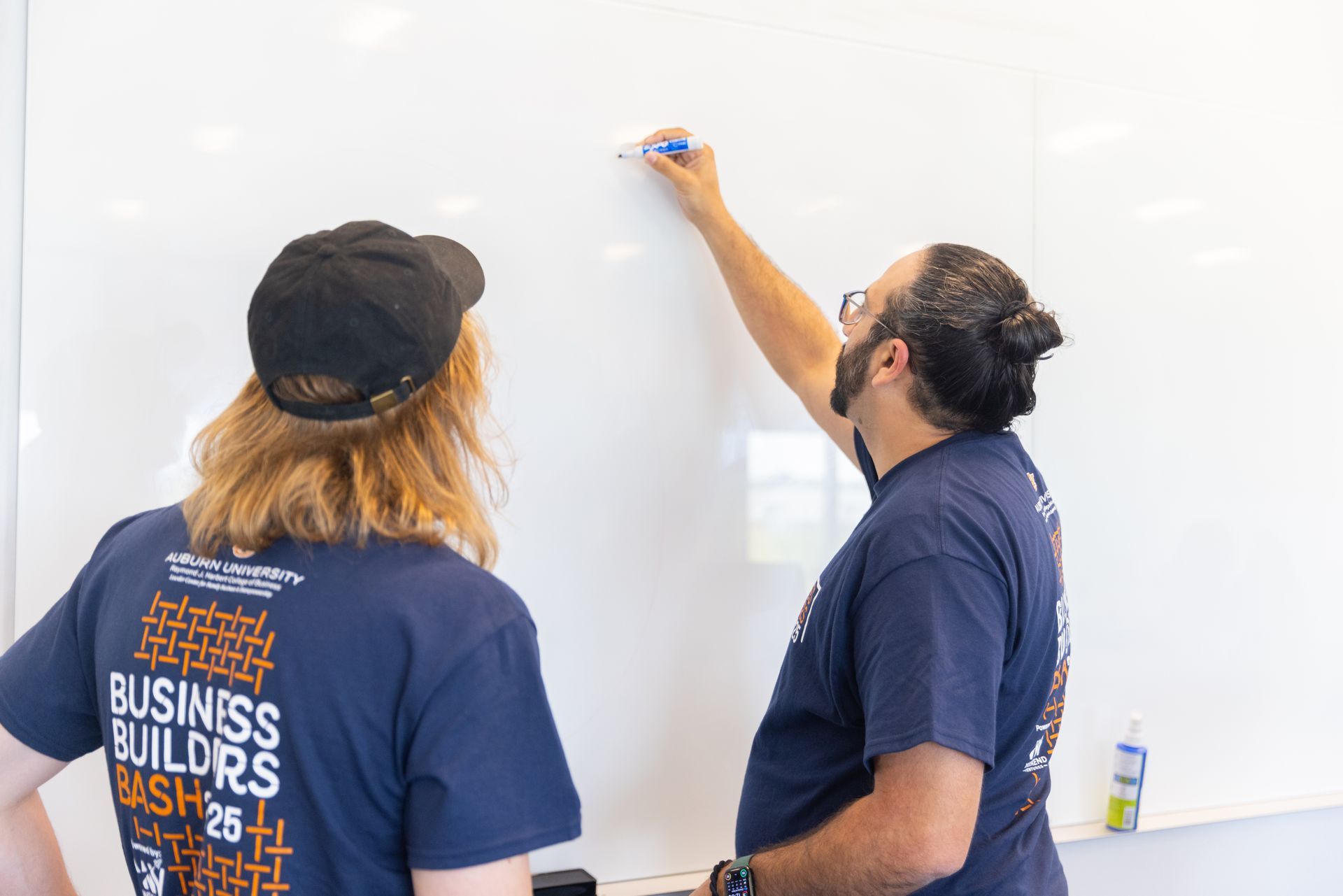 Two people in matching blue shirts stand in front of a whiteboard