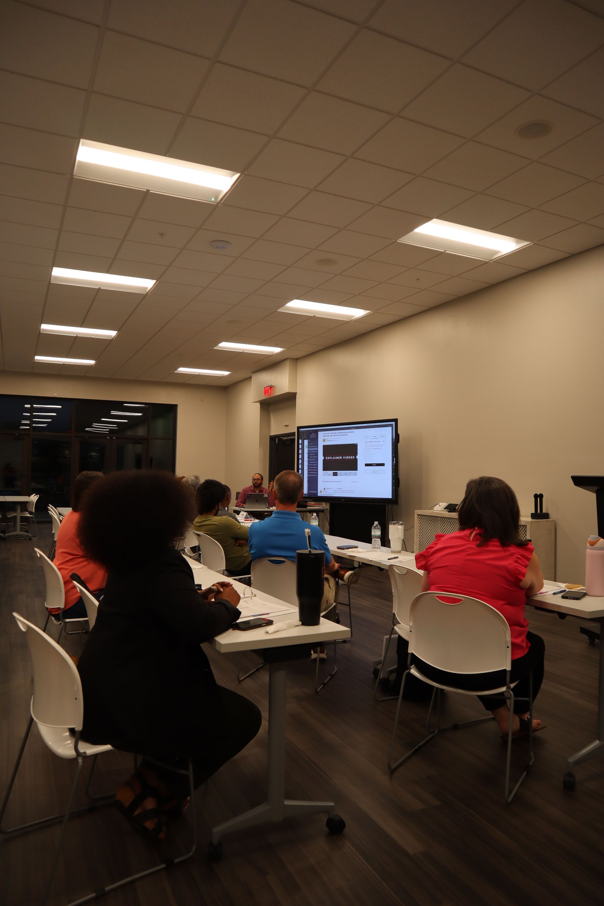 People seated at tables in a classroom, watching a presentation