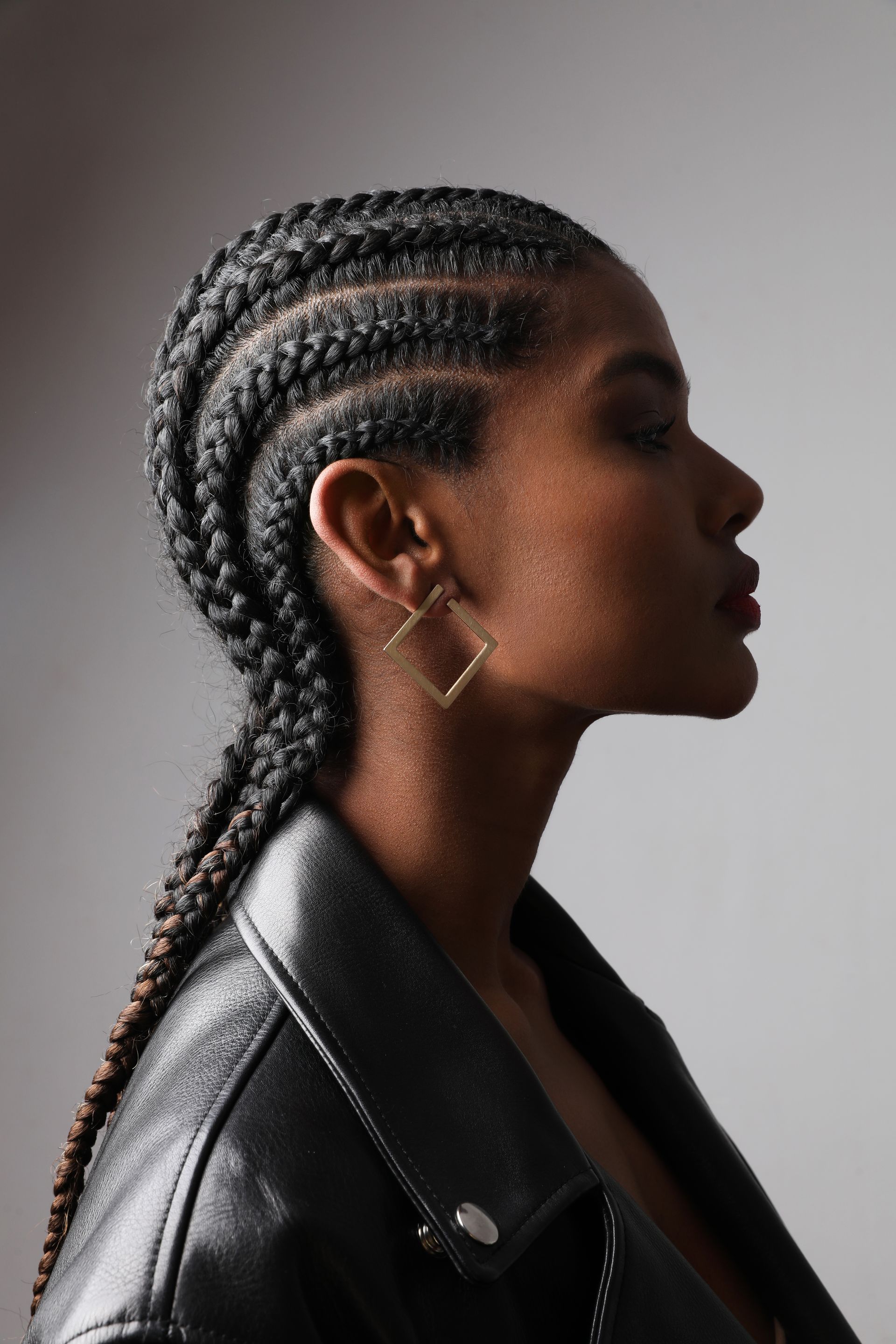 Side profile of a person with braided hair wearing a black leather jacket against a gray background Side profile of a person with braided hair wearing a black leather jacket against a gray background